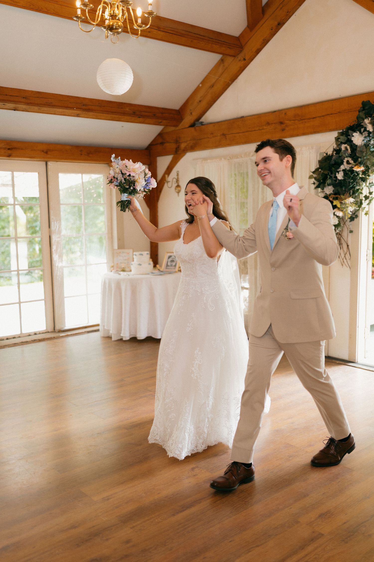 Couple dances playfully in a rustic barn venue with wooden beams and string lights.