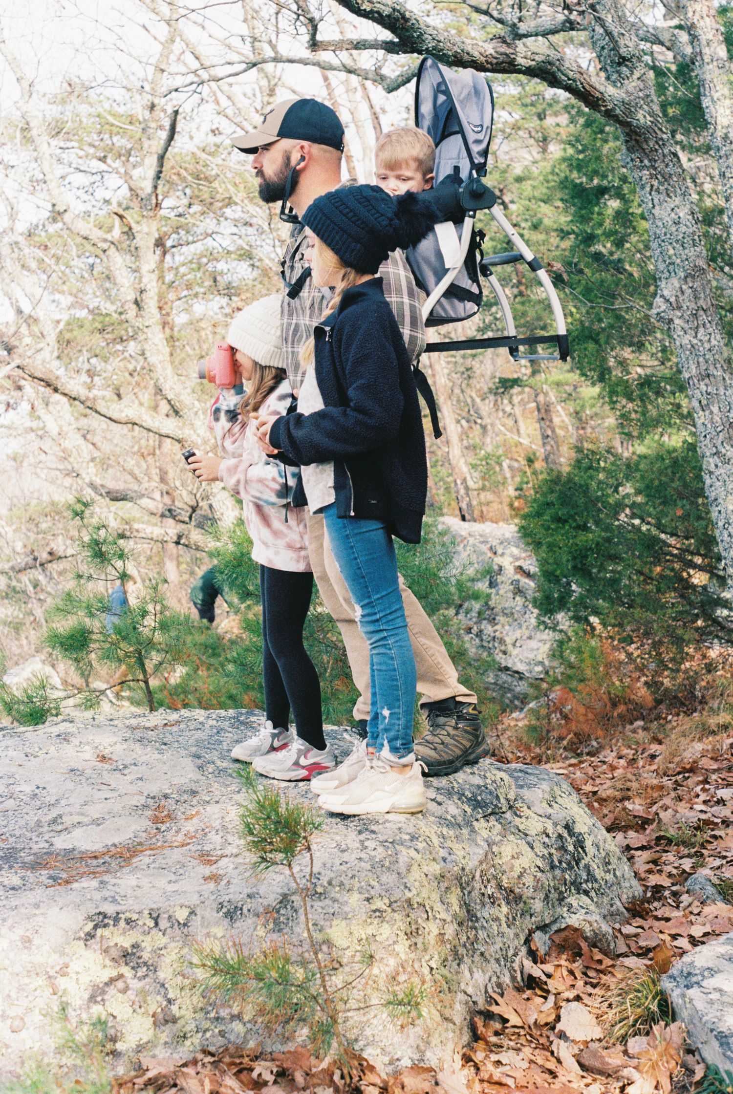 Family exploring rocky trail through autumn forest with fallen leaves.