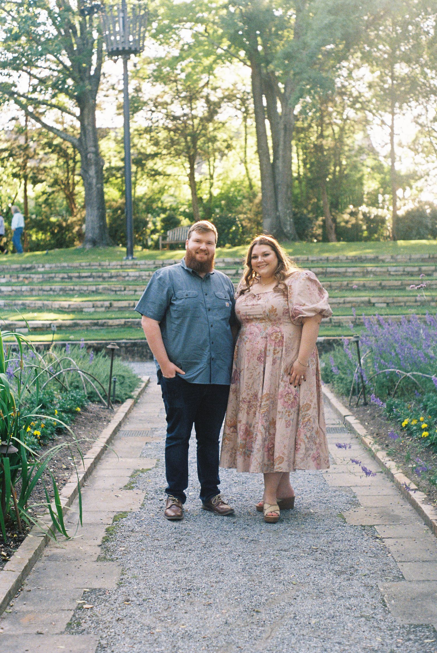 Couple walking along a gravel path in a garden setting during golden hour.