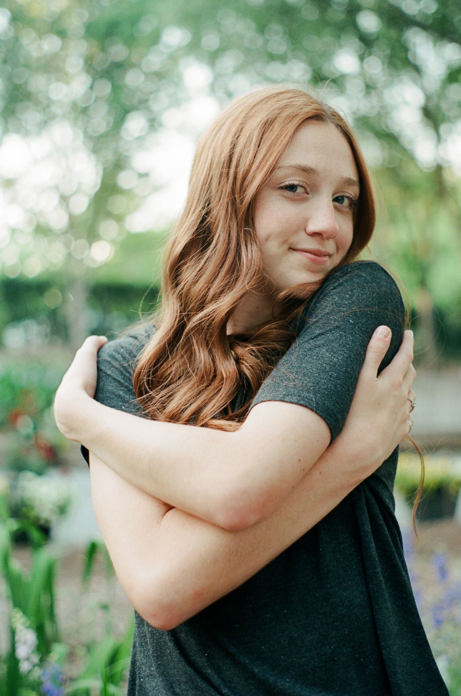 Self-hug portrait sequence in natural outdoor setting with soft bokeh background.