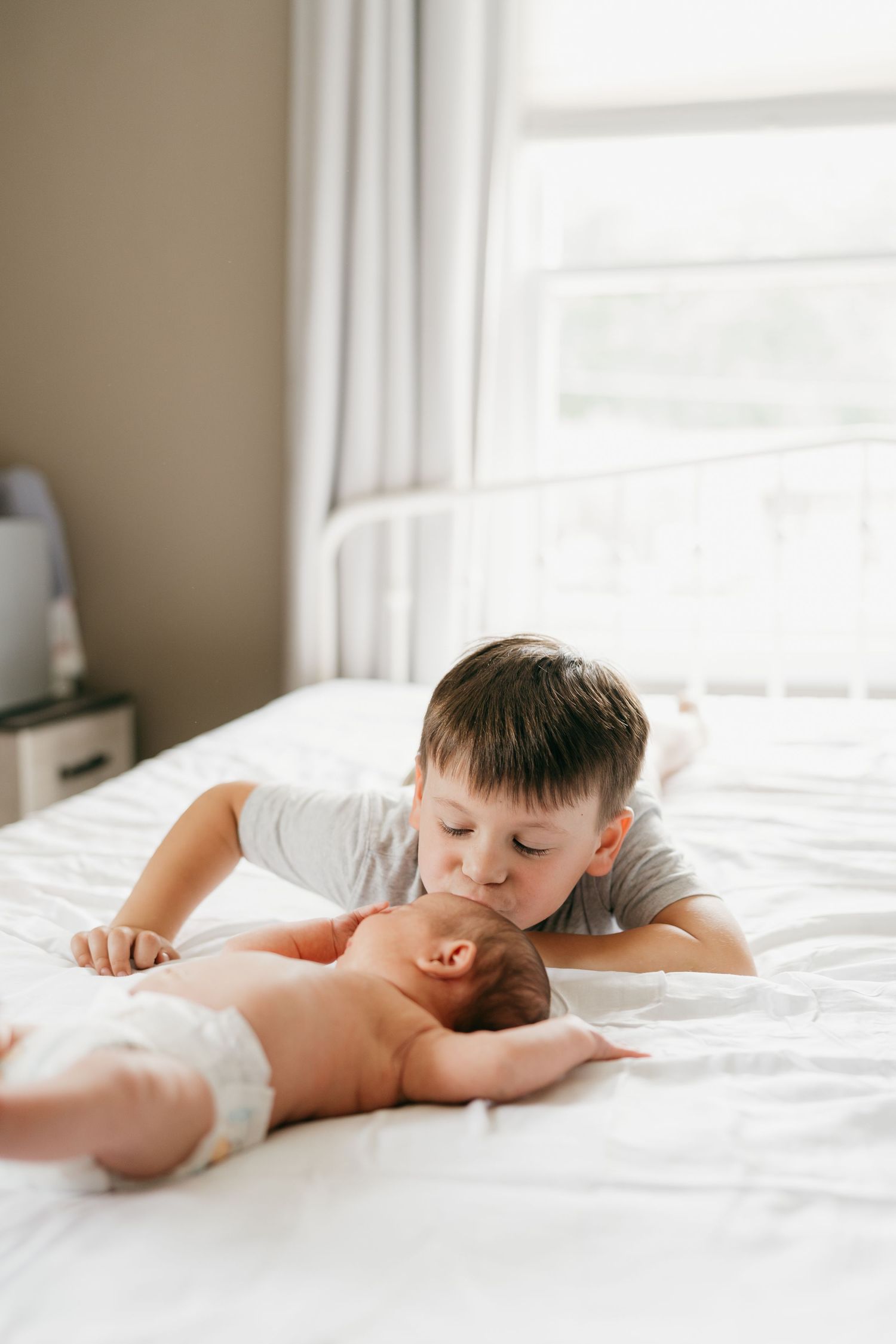 Child resting peacefully on white bedding in natural window light.