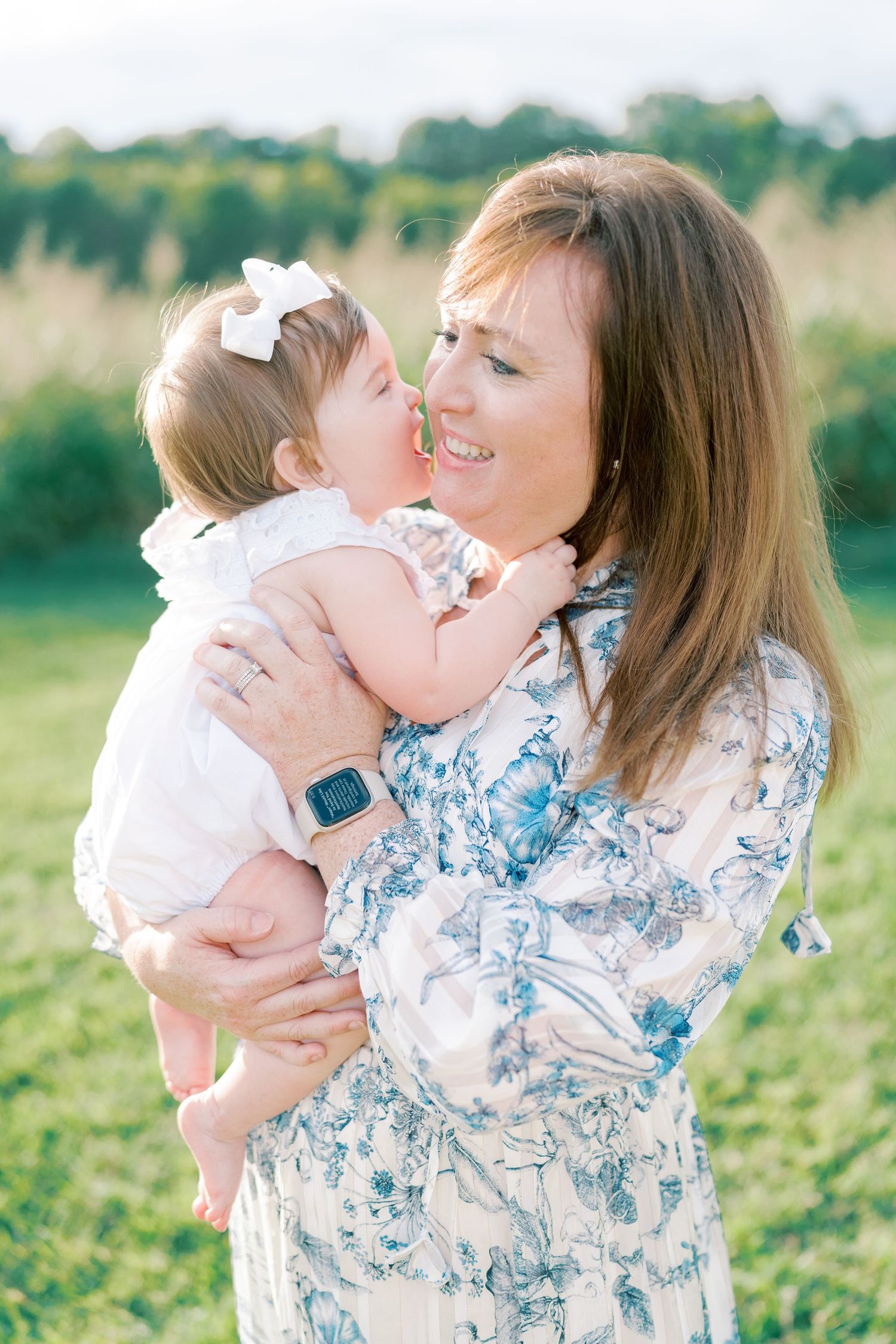 Mother and baby share joyful moments together in a sunny field wearing blue and white outfits.