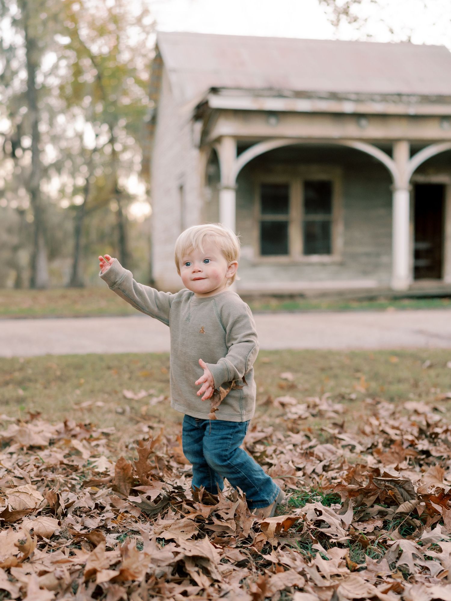 A toddler explores and plays in fallen leaves during autumn.