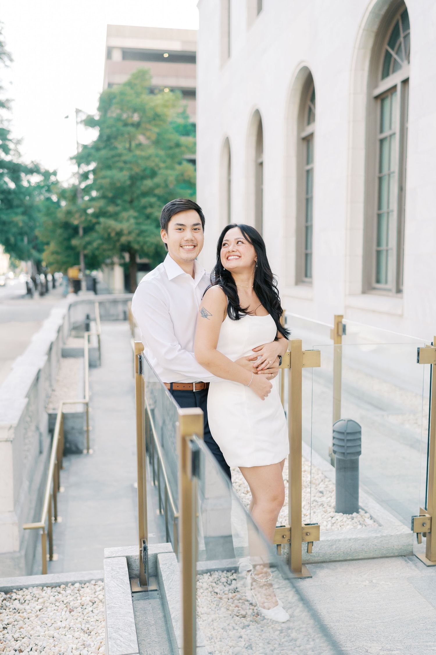 A couple in coordinated white and navy outfits shares joyful moments along an outdoor walkway.