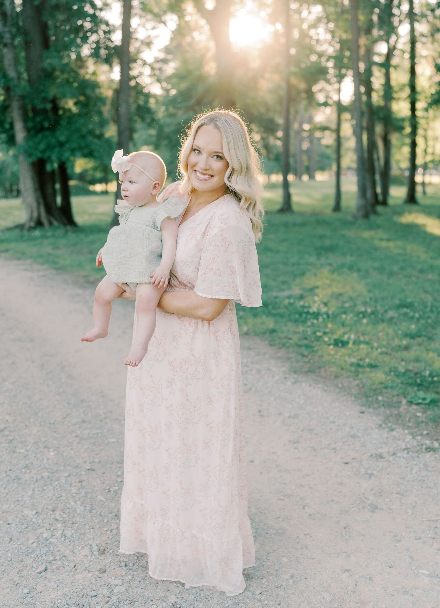 A family walks along a sunlit forest path in soft pink and neutral clothing.