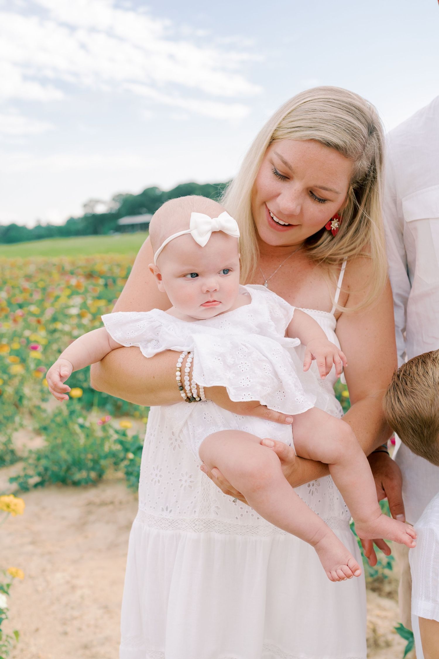 Baby in white dress being held in a flower field during summer photo session.