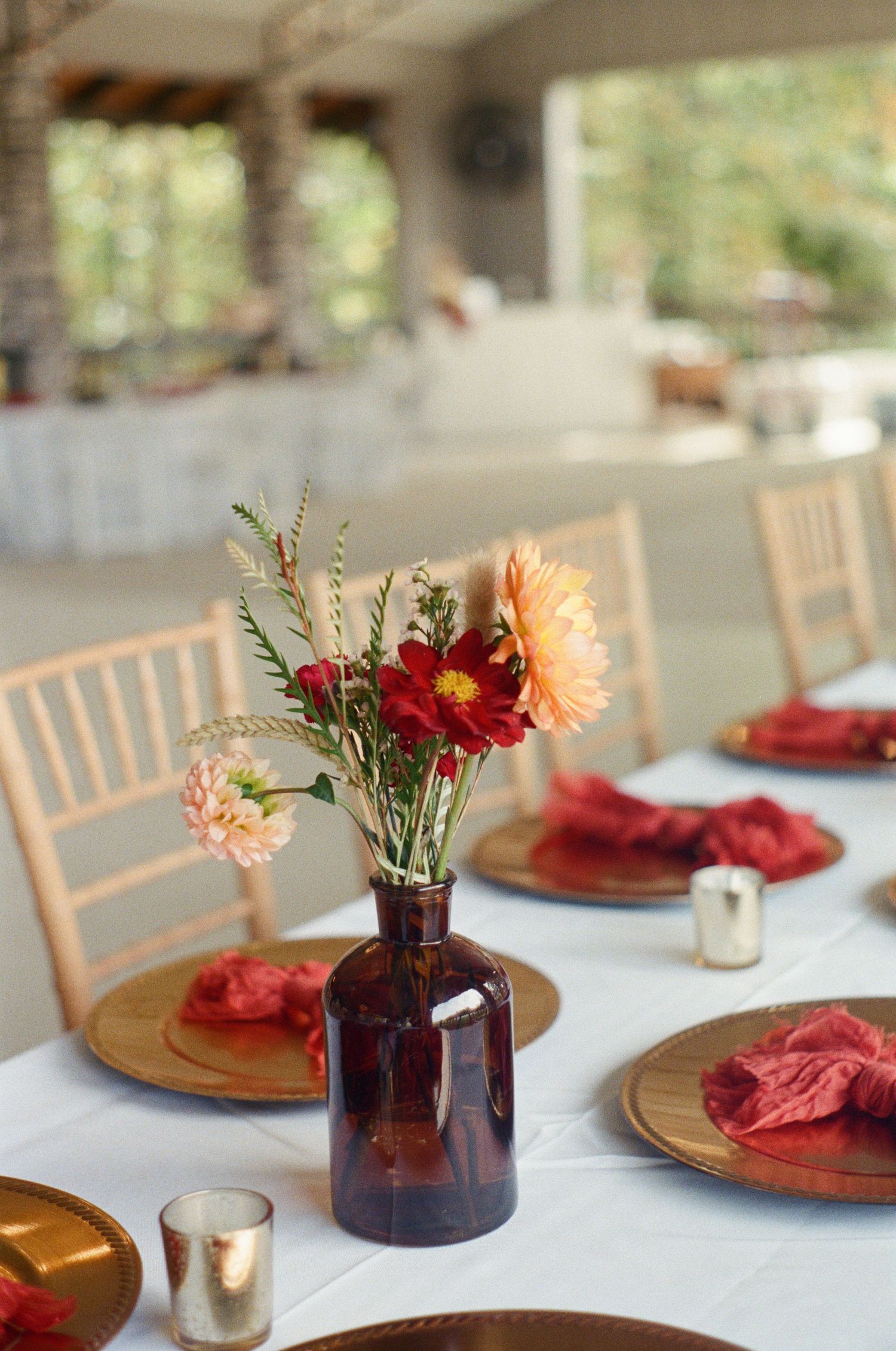 Wedding table settings with burgundy plates and amber glass vase centerpieces.