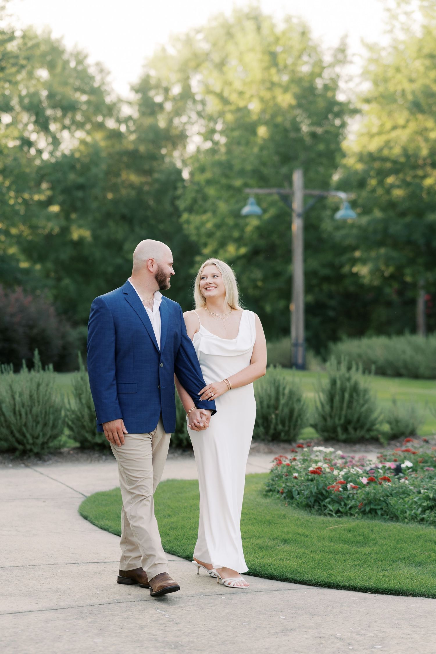 Couple strolling through garden path with blooming flowers.
