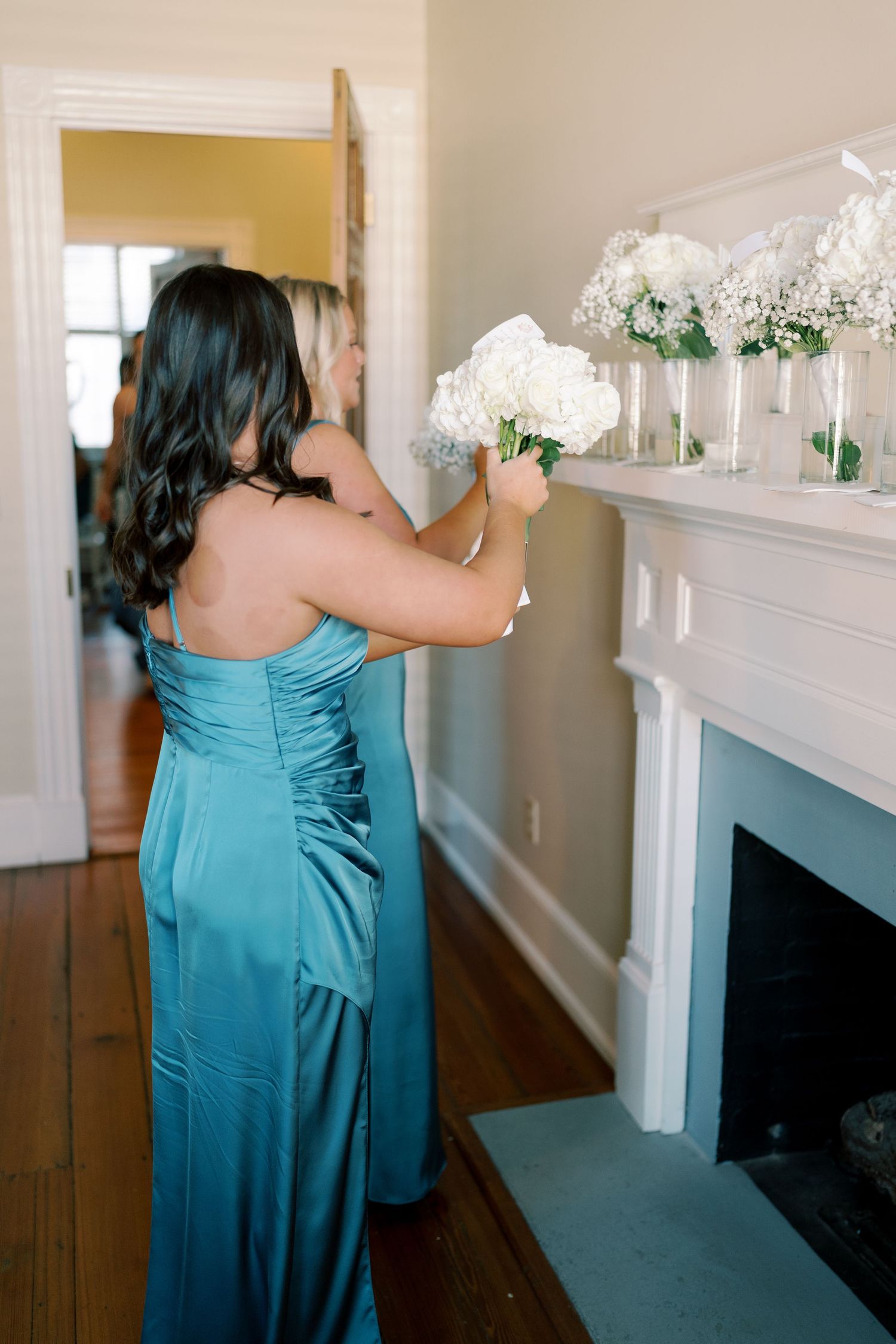 Wedding decorations being arranged on a white mantle with floral accents and greenery.
