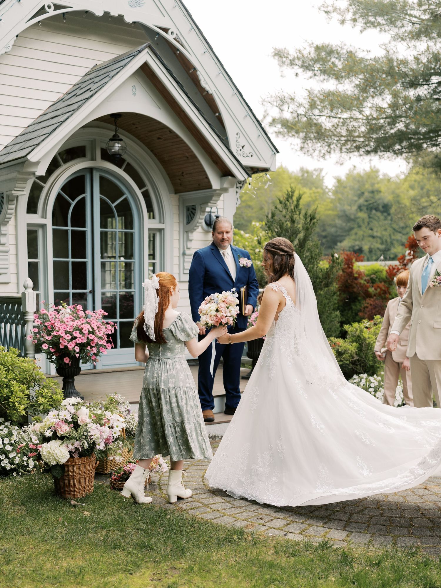 Elegant wedding scene with flowing white dress against stone chapel backdrop adorned with pink flowers.