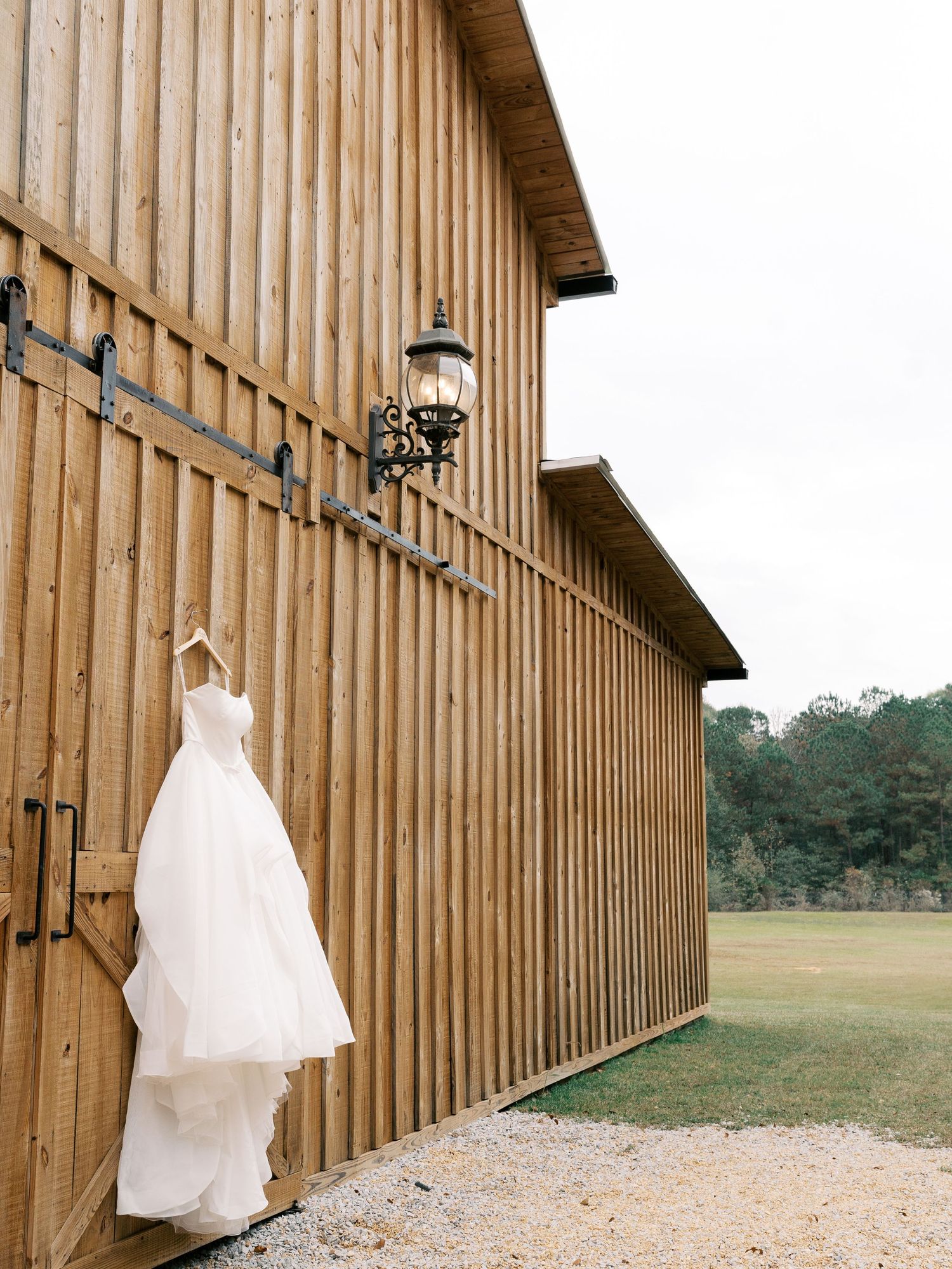 White wedding dress hanging on wooden barn wall in natural outdoor setting.