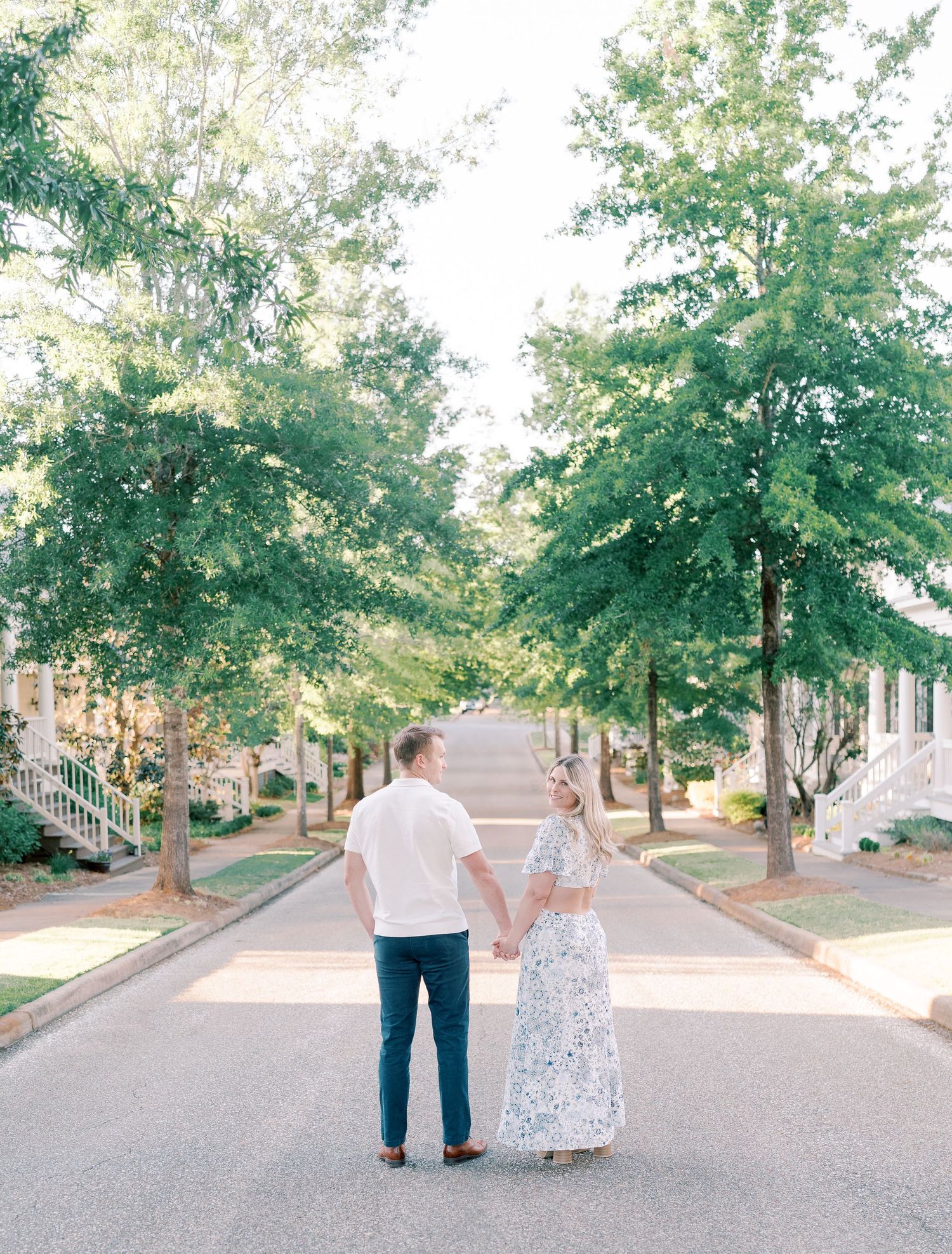 Couple walks hand in hand down tree-lined path in summer setting.