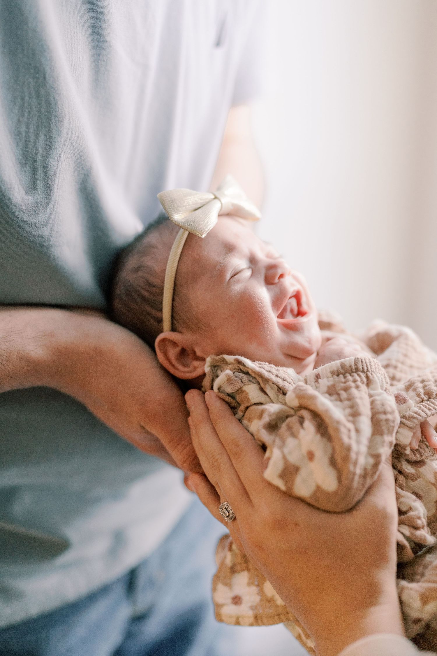 A peaceful sleeping baby wearing a bow headband rests in gentle arms.