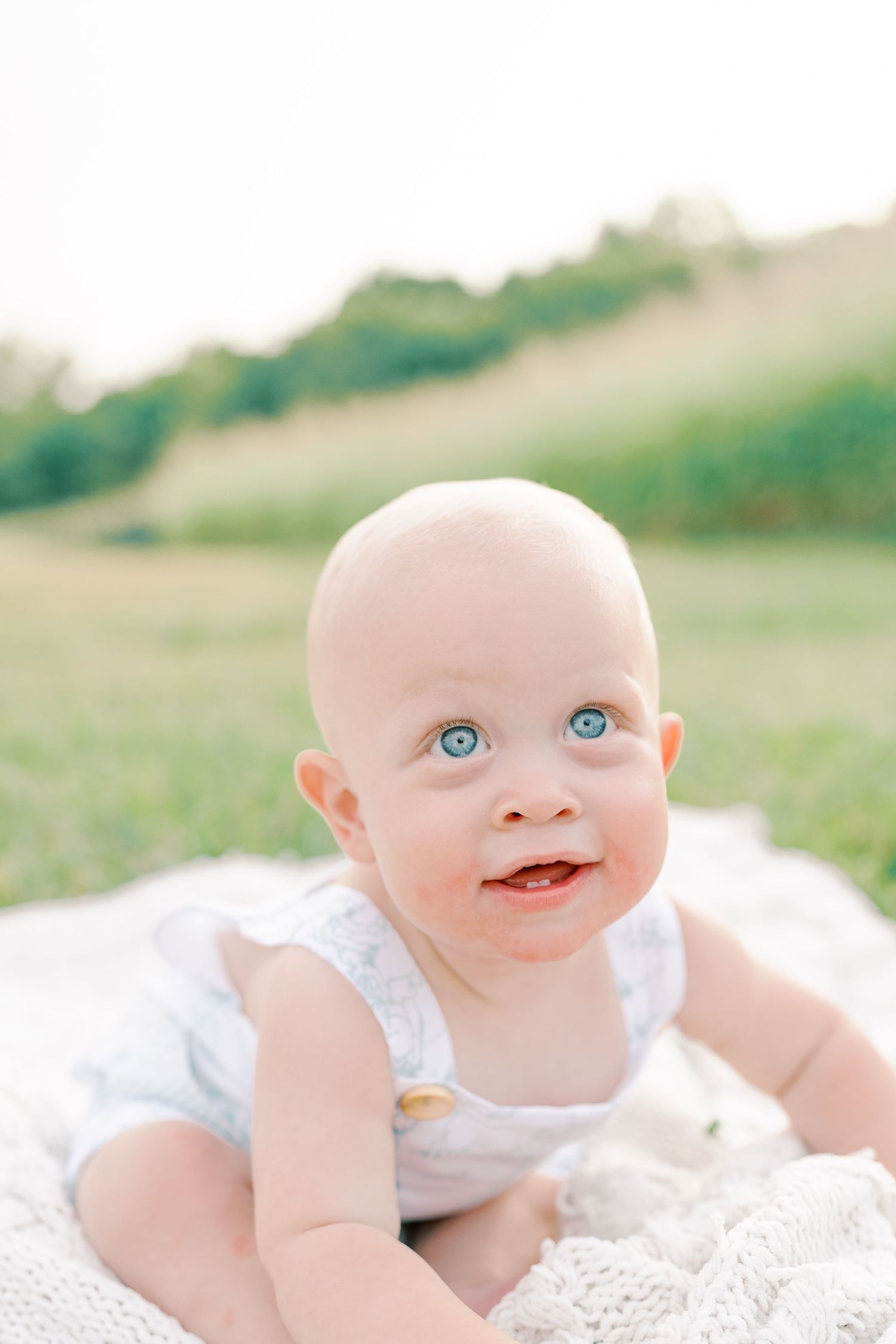 Close-up portraits of smiling baby with bright blue eyes on white blanket outdoors.