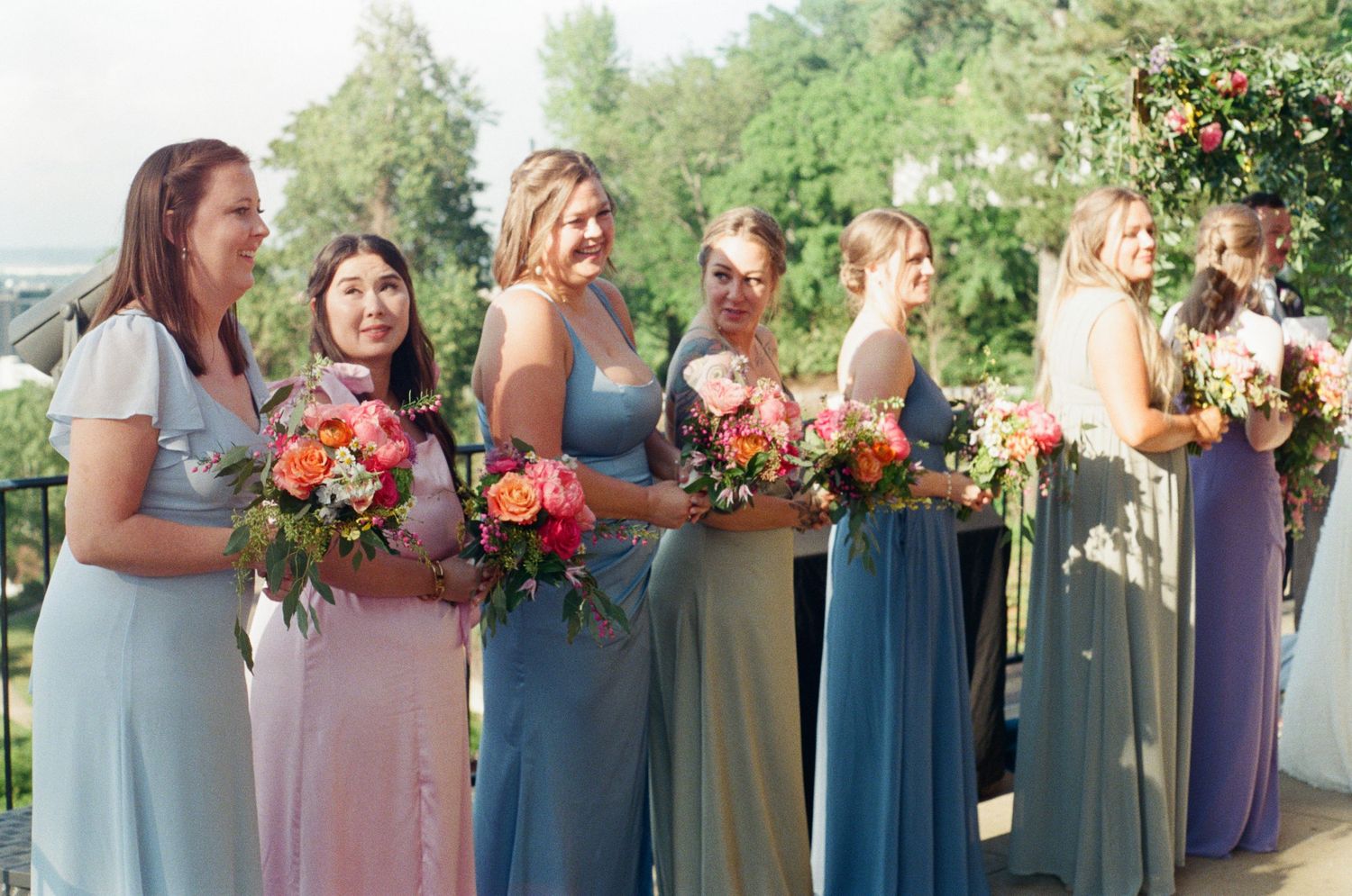 Bridesmaids in pastel dresses holding colorful bouquets at an outdoor wedding.