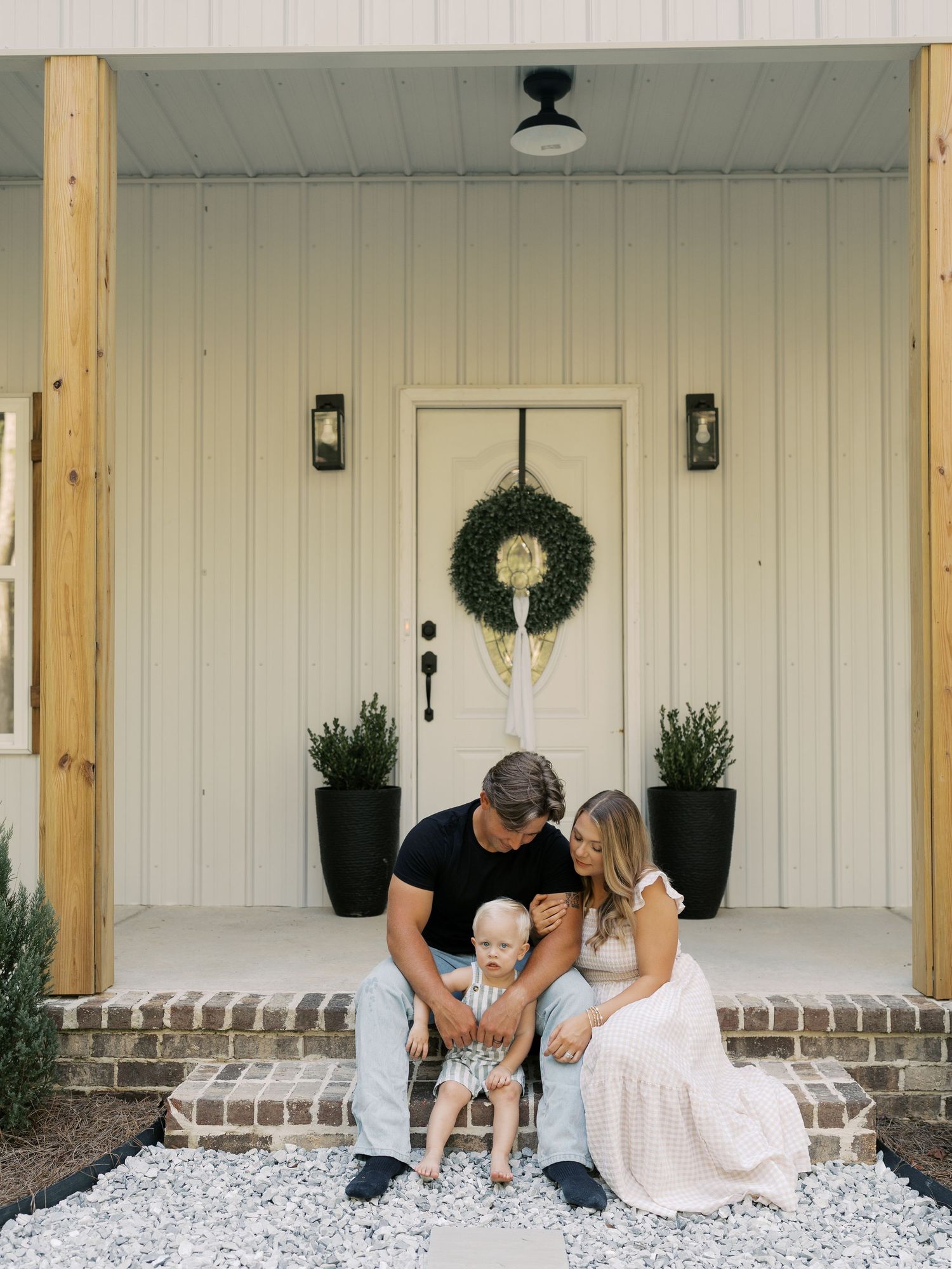 Family relaxes together on white stone porch with decorative greenery.