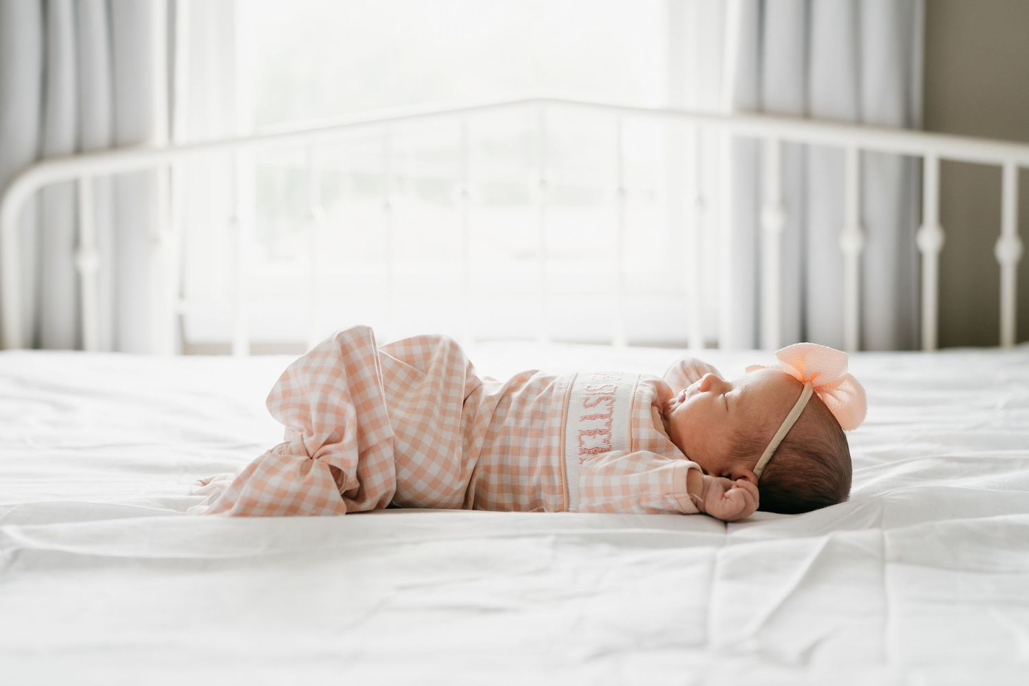 Newborn baby sleeping soundly on white bedding in natural light.