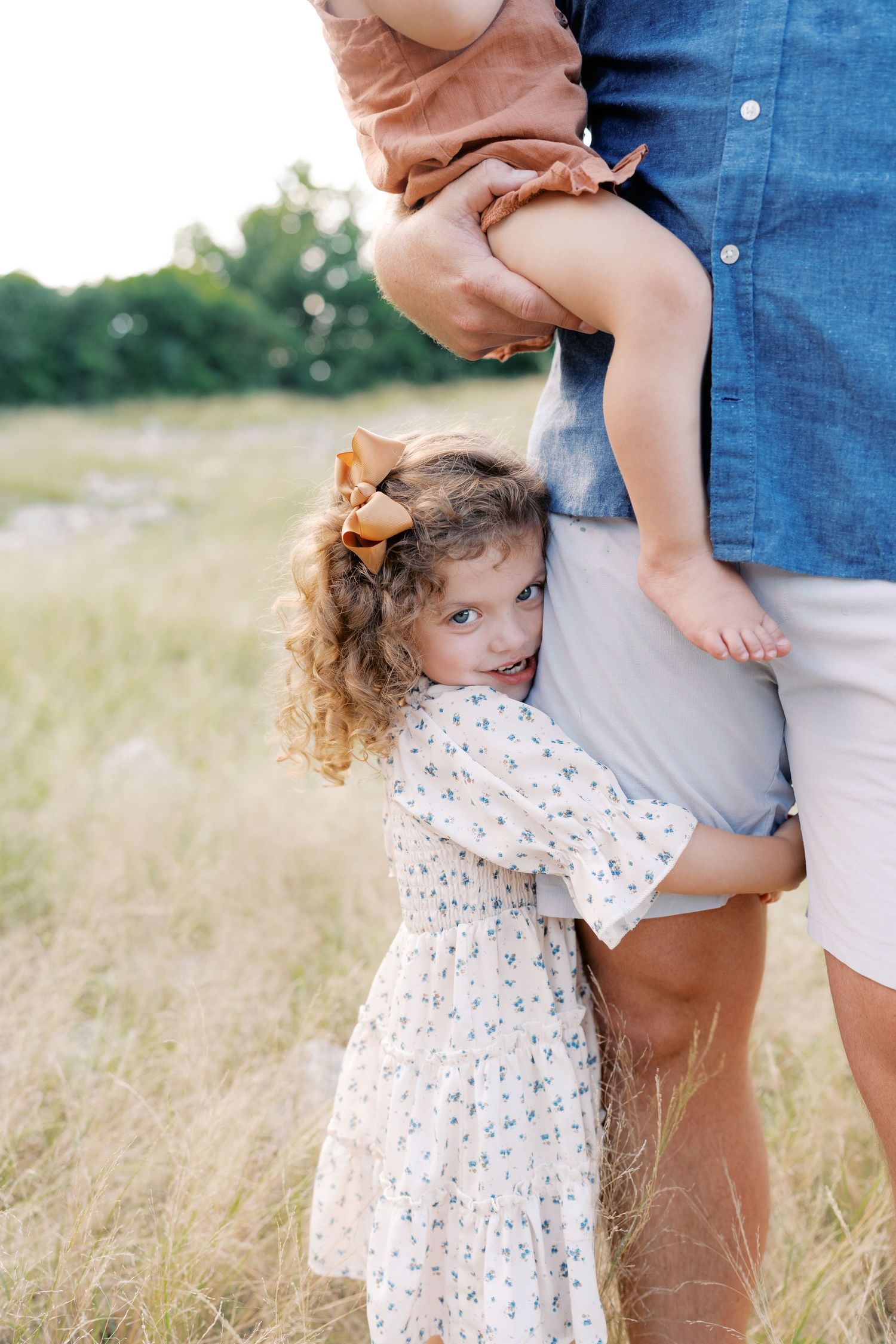 Sweet candid moment of family members embracing in a sunlit meadow.