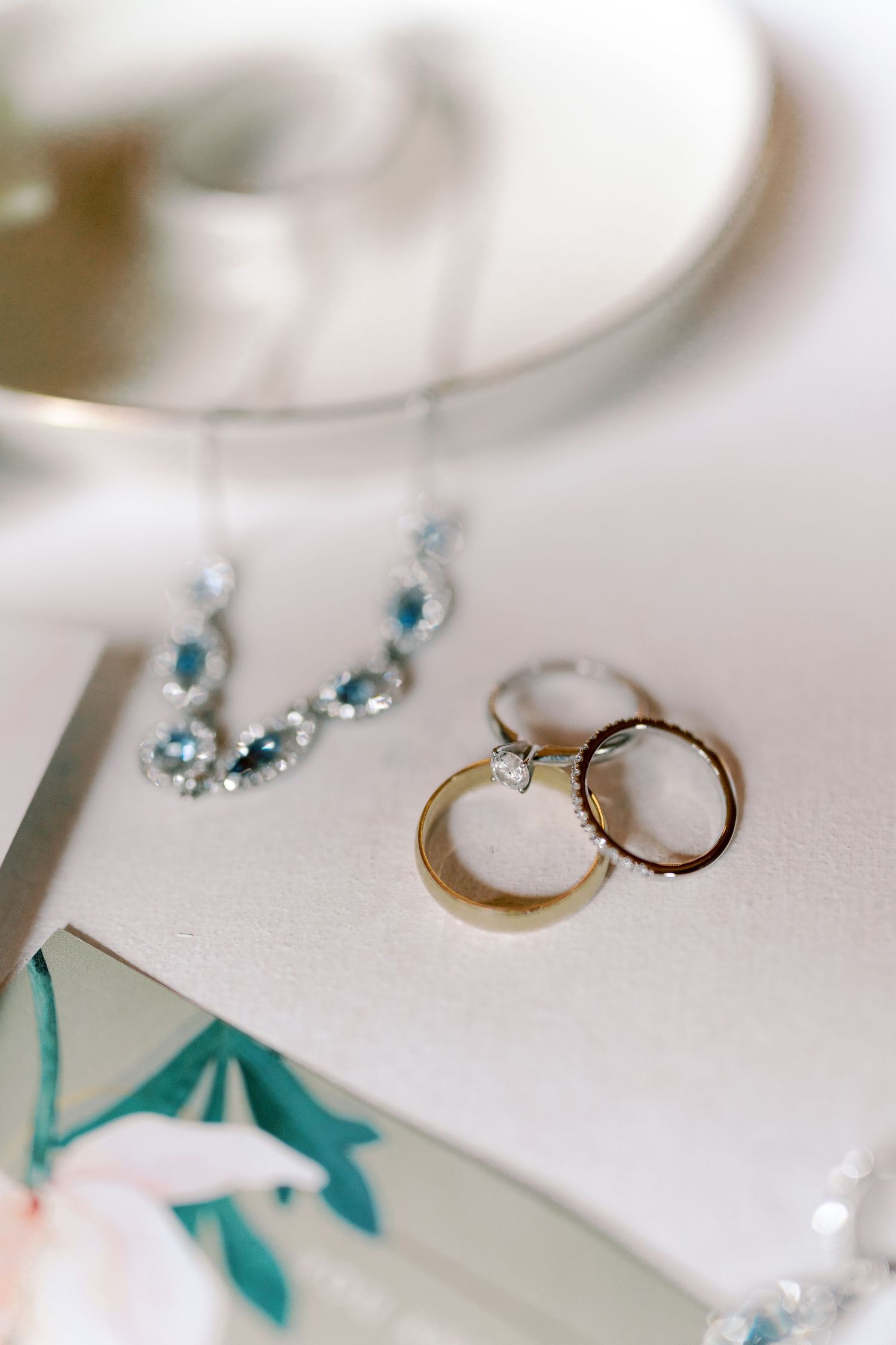 Wedding jewelry including rings and blue crystal accessories on white surface.