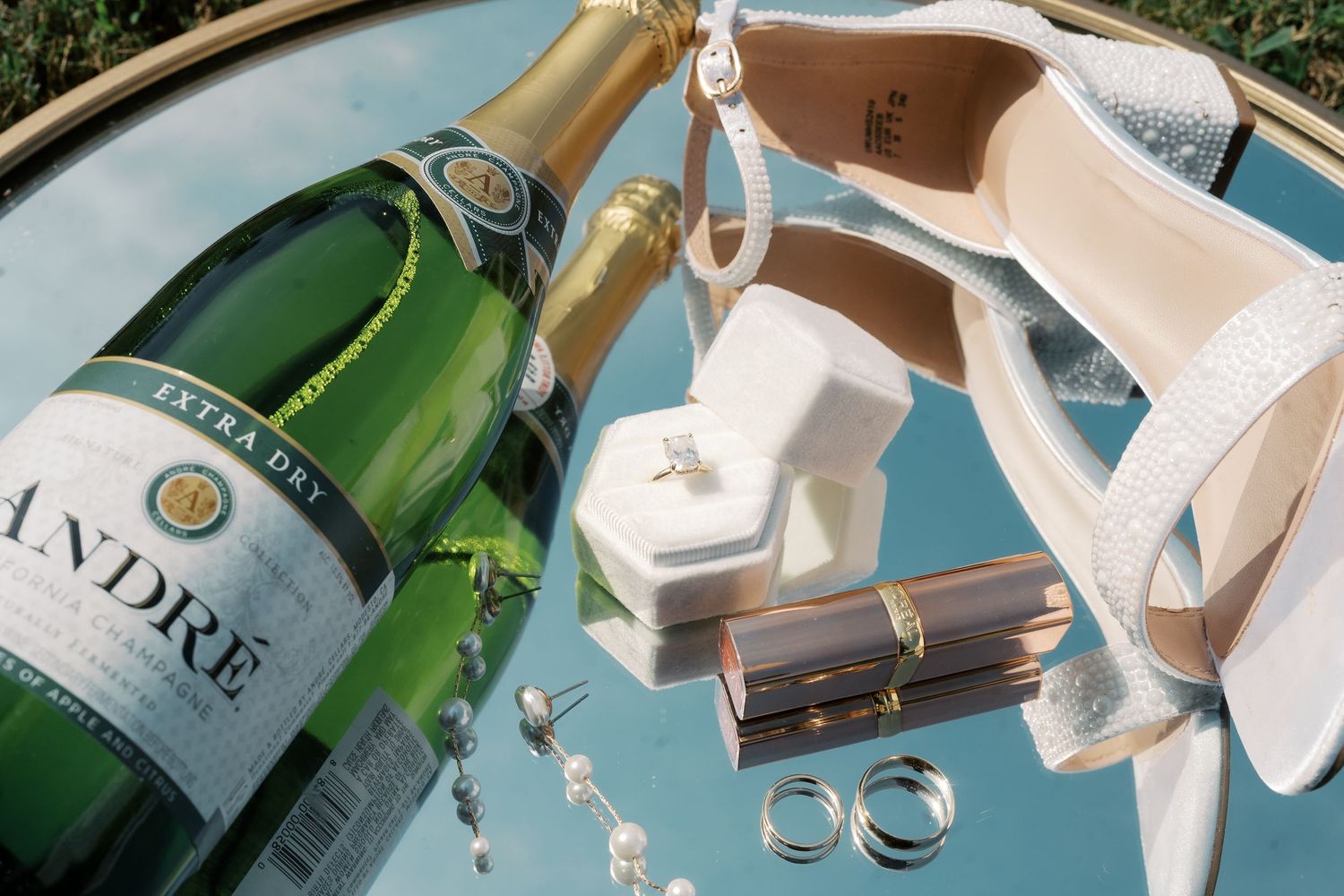Wedding rings, champagne bottles and accessories arranged artistically on a blue reflective surface.