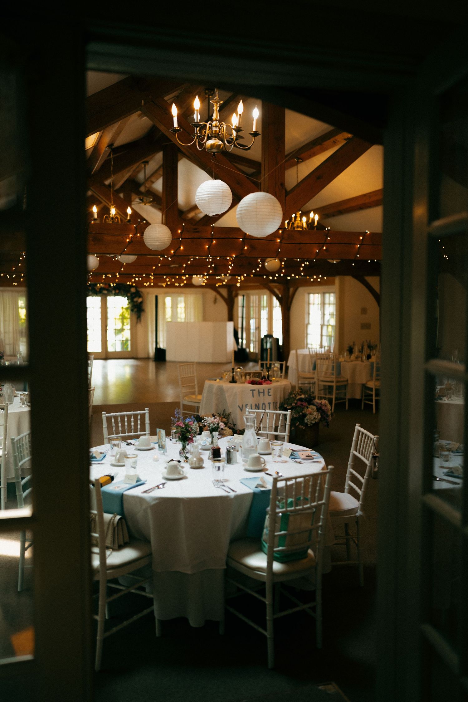 Elegant wedding reception venue with white tablecloths and twinkling lights on wooden beams.