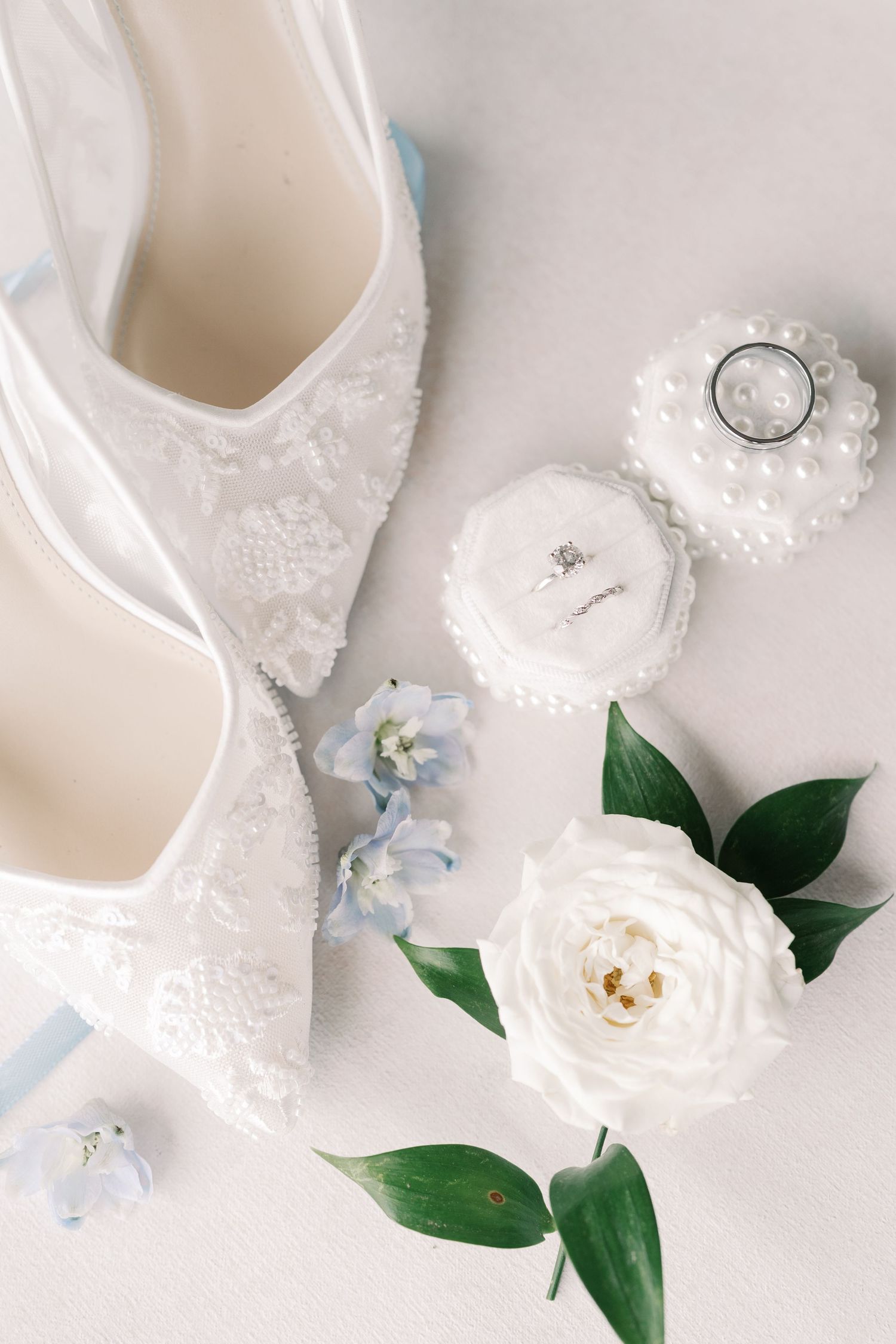 White bridal shoes with lace details and floral accents arranged on light background.