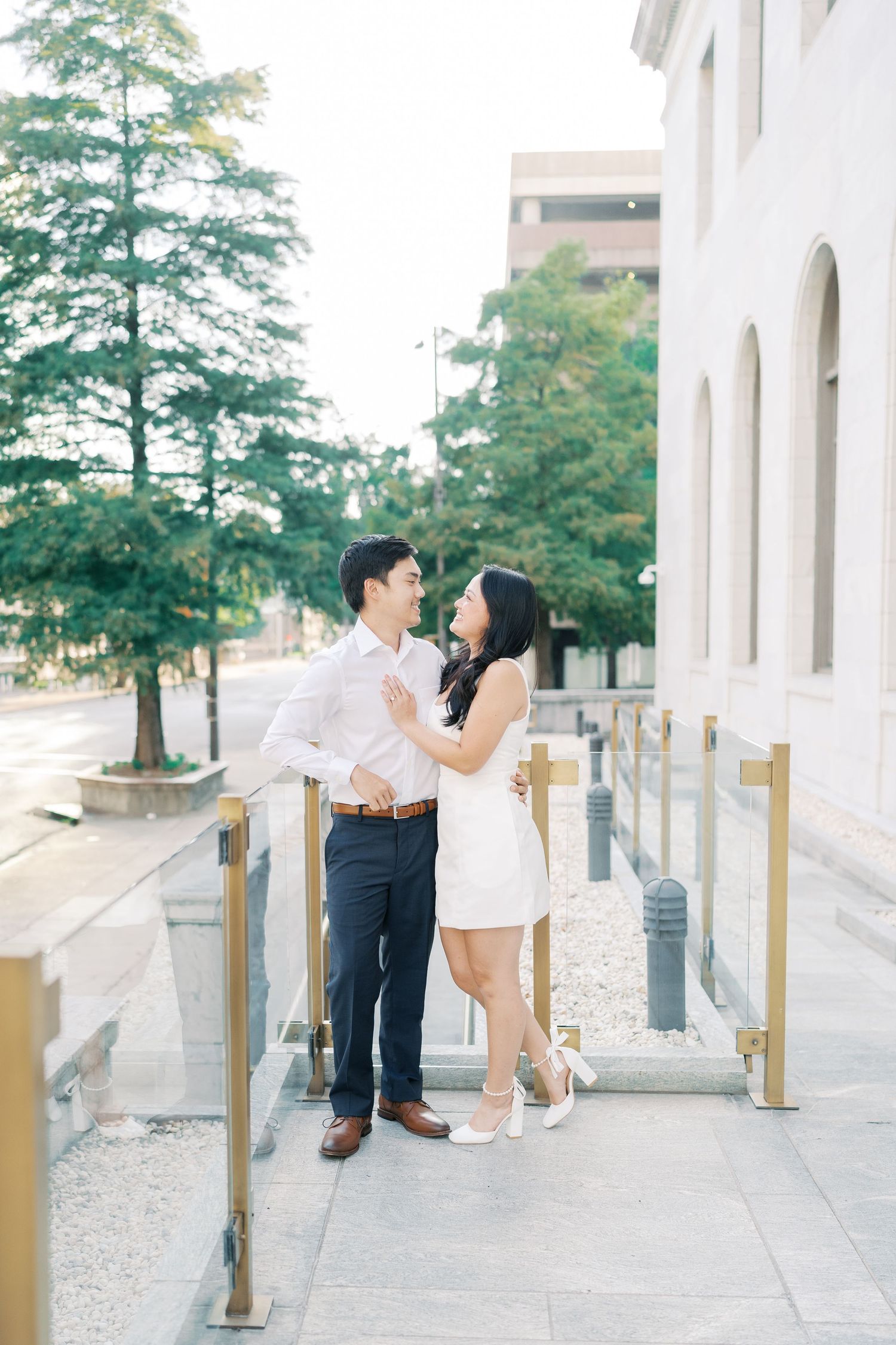 A couple shares candid moments along an architectural walkway with gold safety posts.