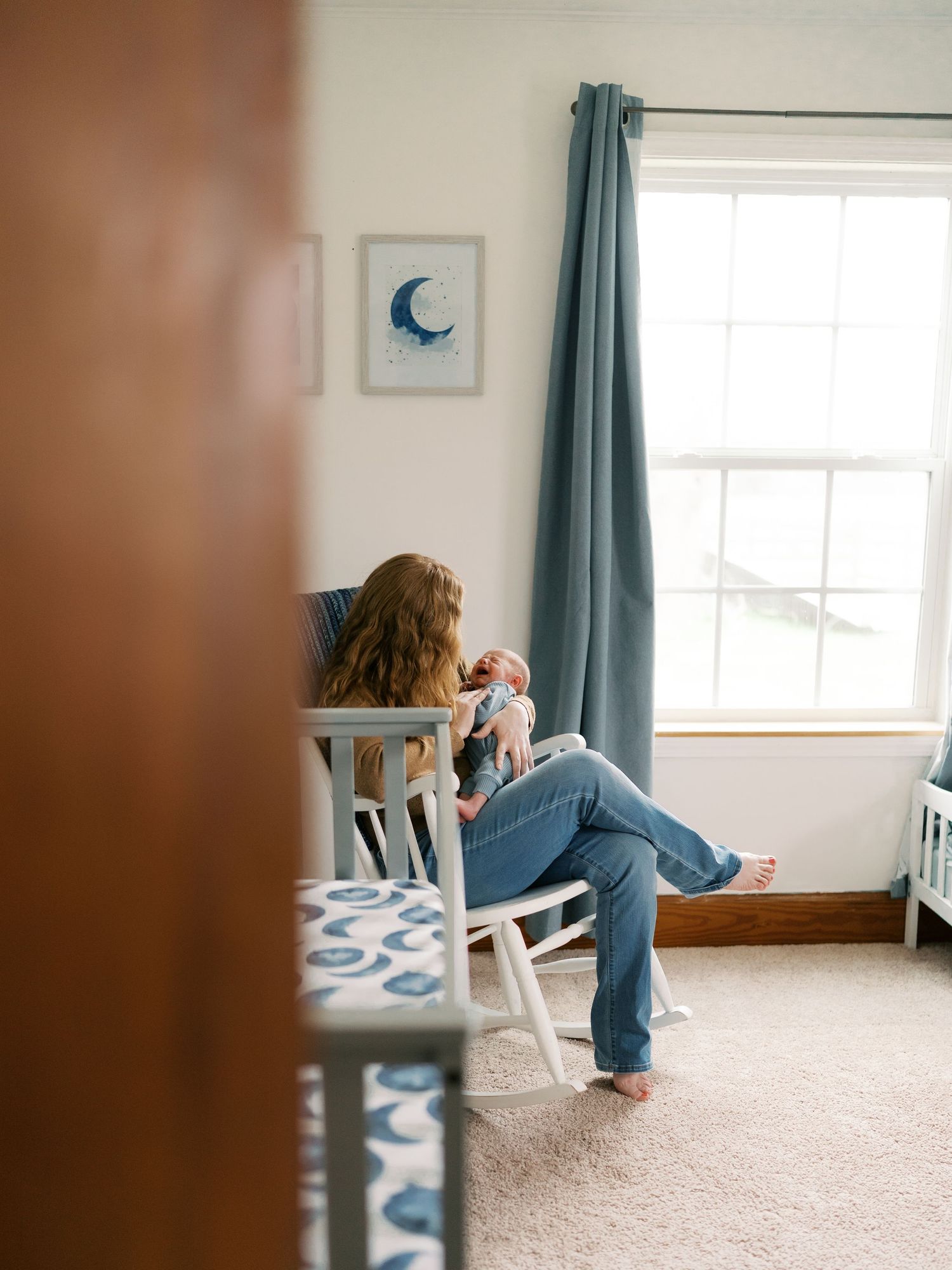 Candid family moment in nursery with white crib and teal curtains.