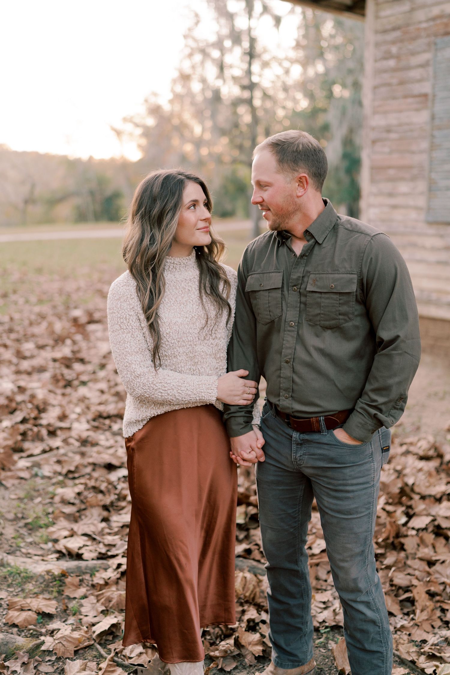 A couple shares a romantic moment among fallen autumn leaves outside a brick building.