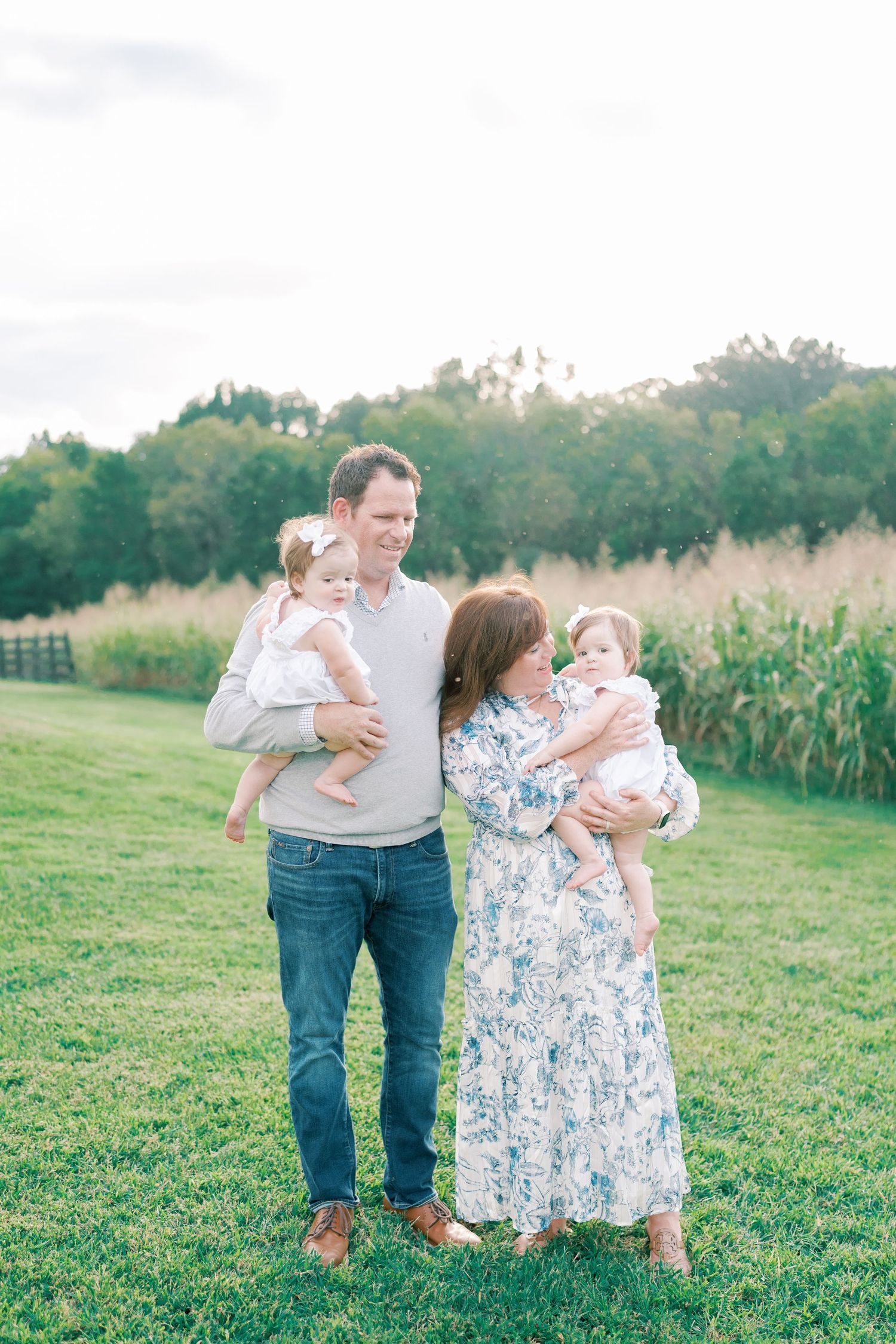 A family shares loving moments while walking through a grassy field near a cornfield.