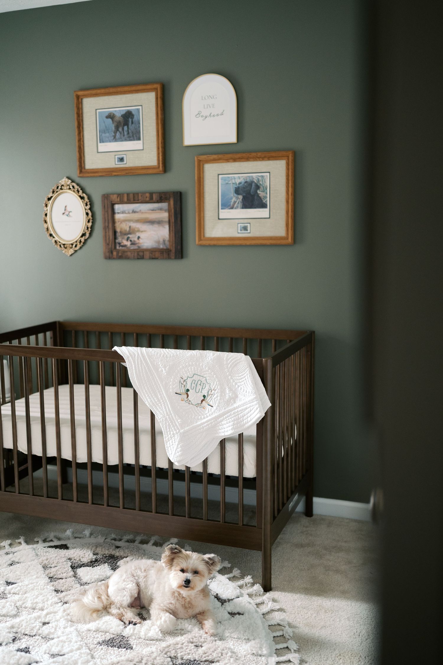 Dark green nursery room with wooden crib, framed artwork, and white bedding.