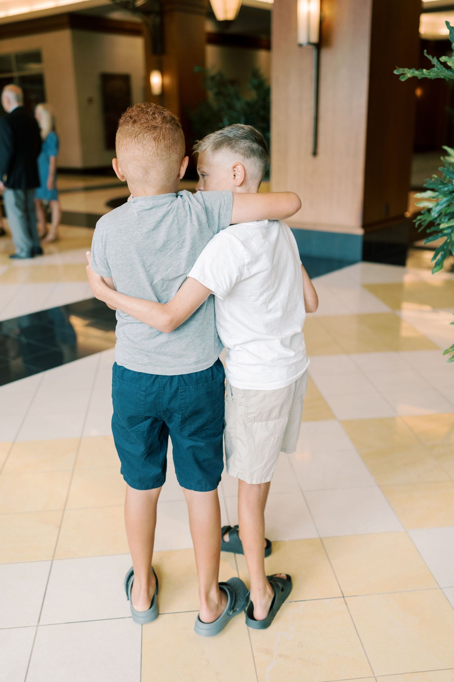 Two children walking together on tiled floor seen from behind.