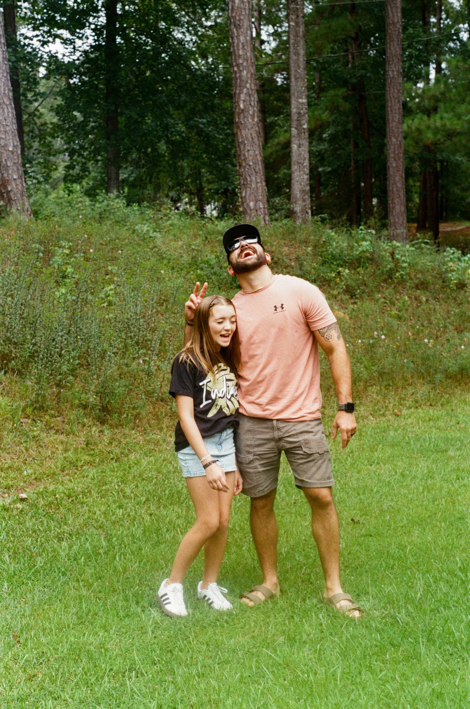 Playful outdoor photo sequence showing people jumping and posing on grass with pine trees in background.
