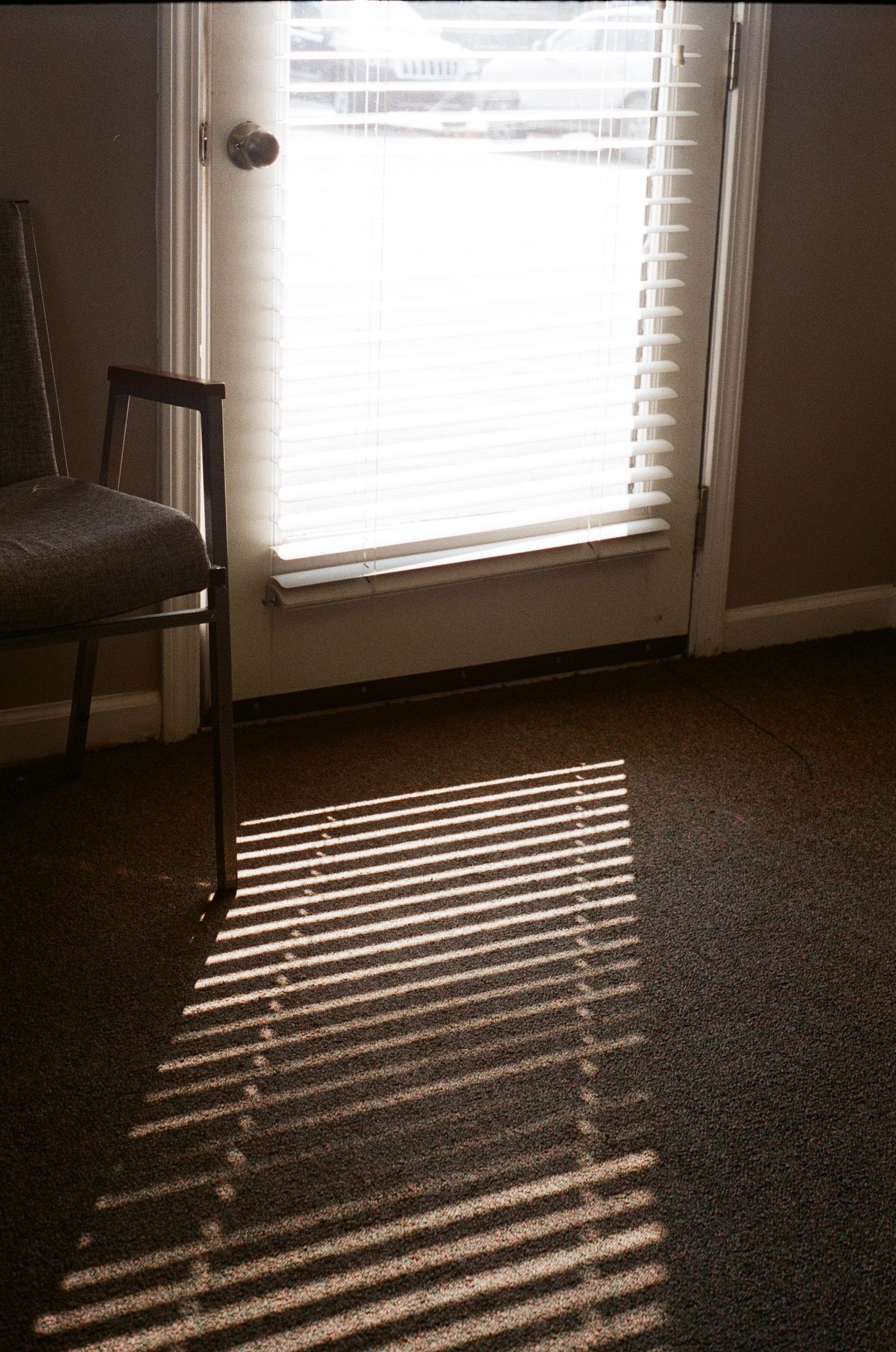Sunlight streaming through horizontal blinds casts parallel lines of light on a dark floor.