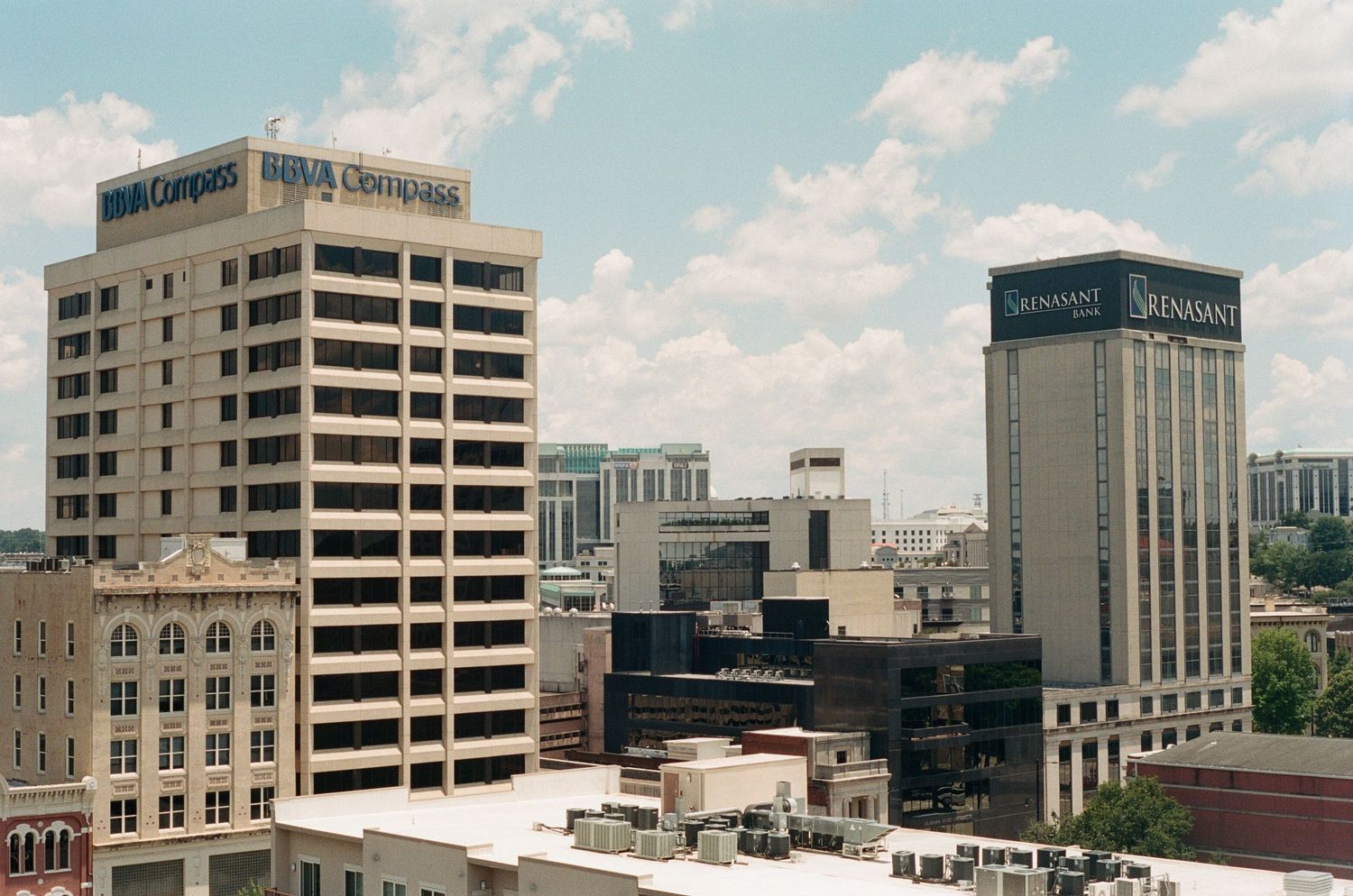 Urban skyline panorama showing office buildings and parking structures against a blue sky.