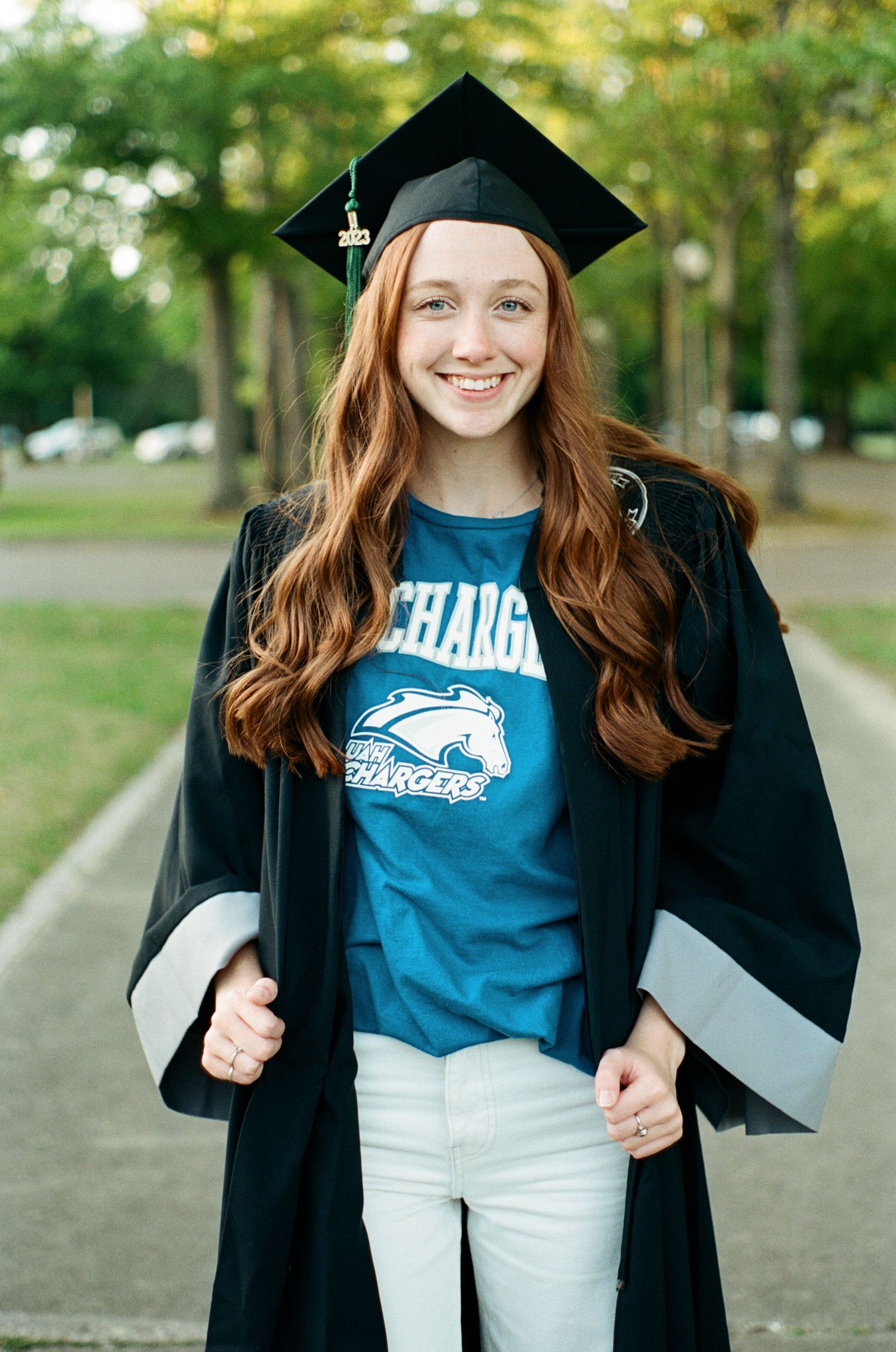 Graduate in cap and gown showing school spirit in blue t-shirt outdoors.