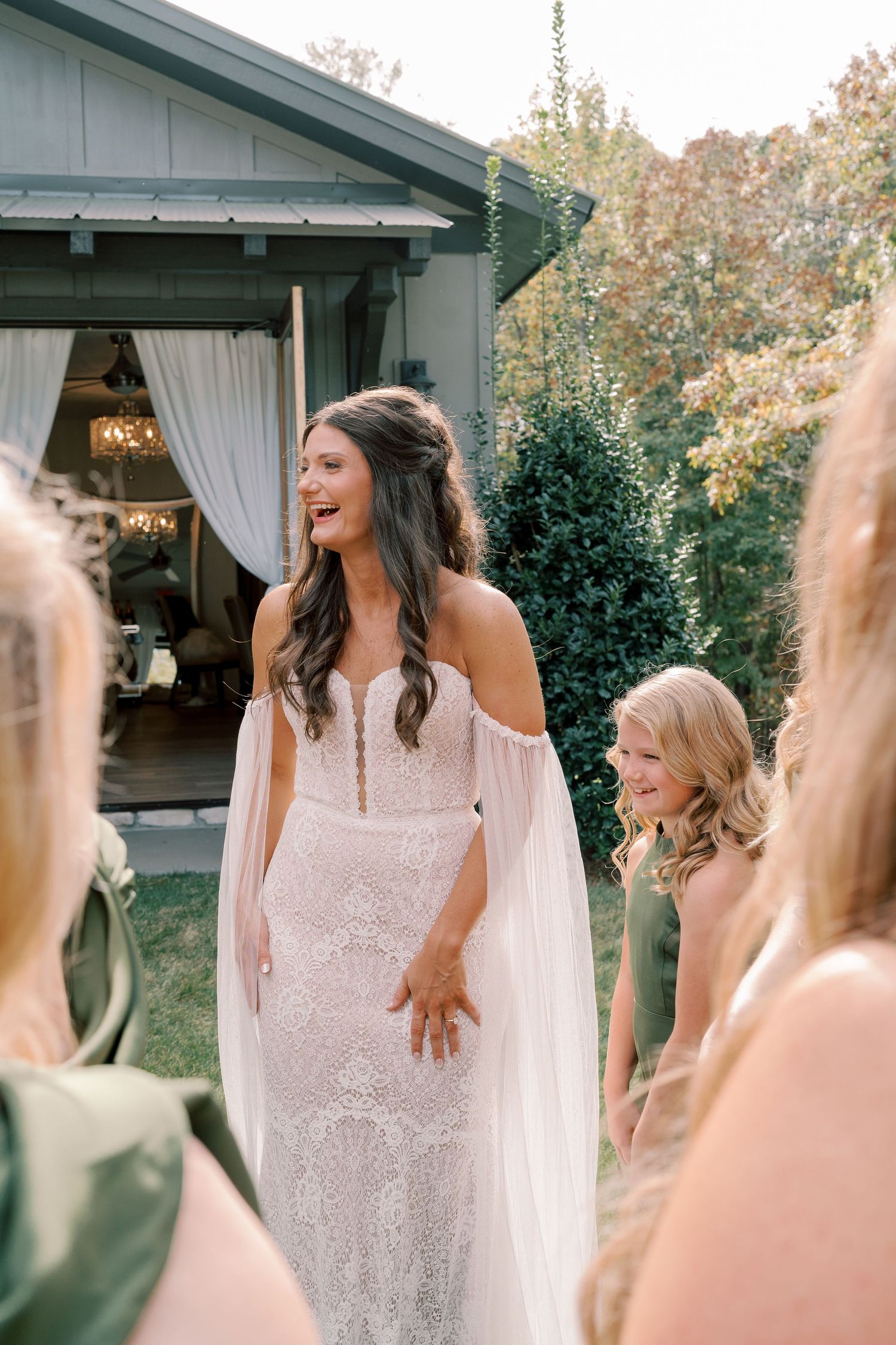 Wedding party shares joyful moments outside a venue with greenery in the background.