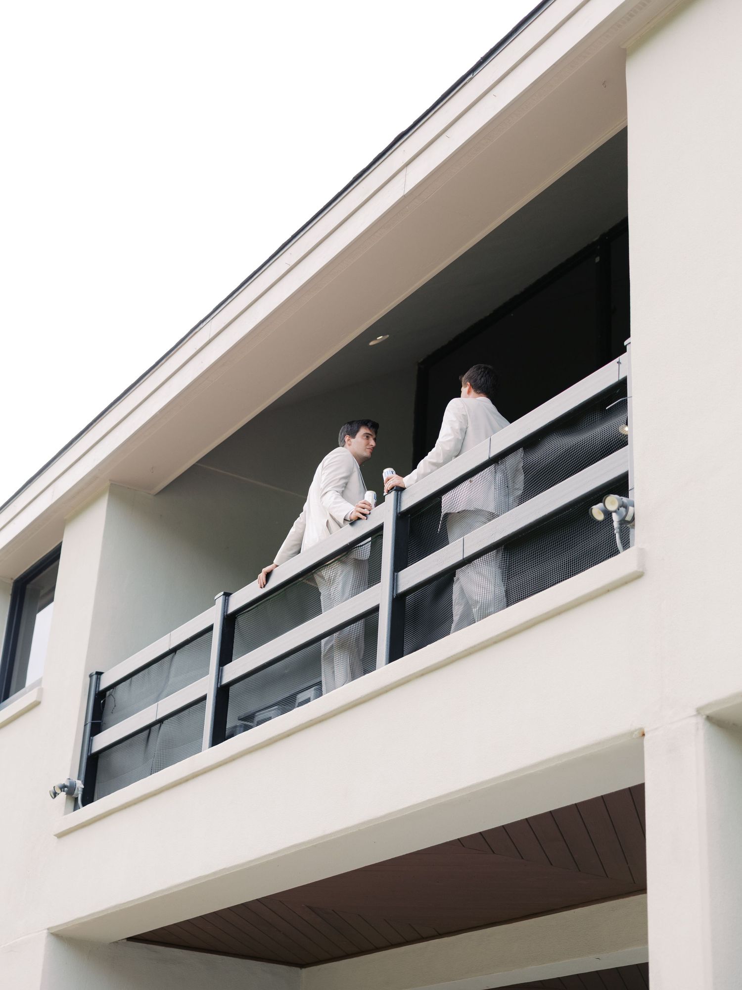 Two people in formal attire standing on a modern white balcony.