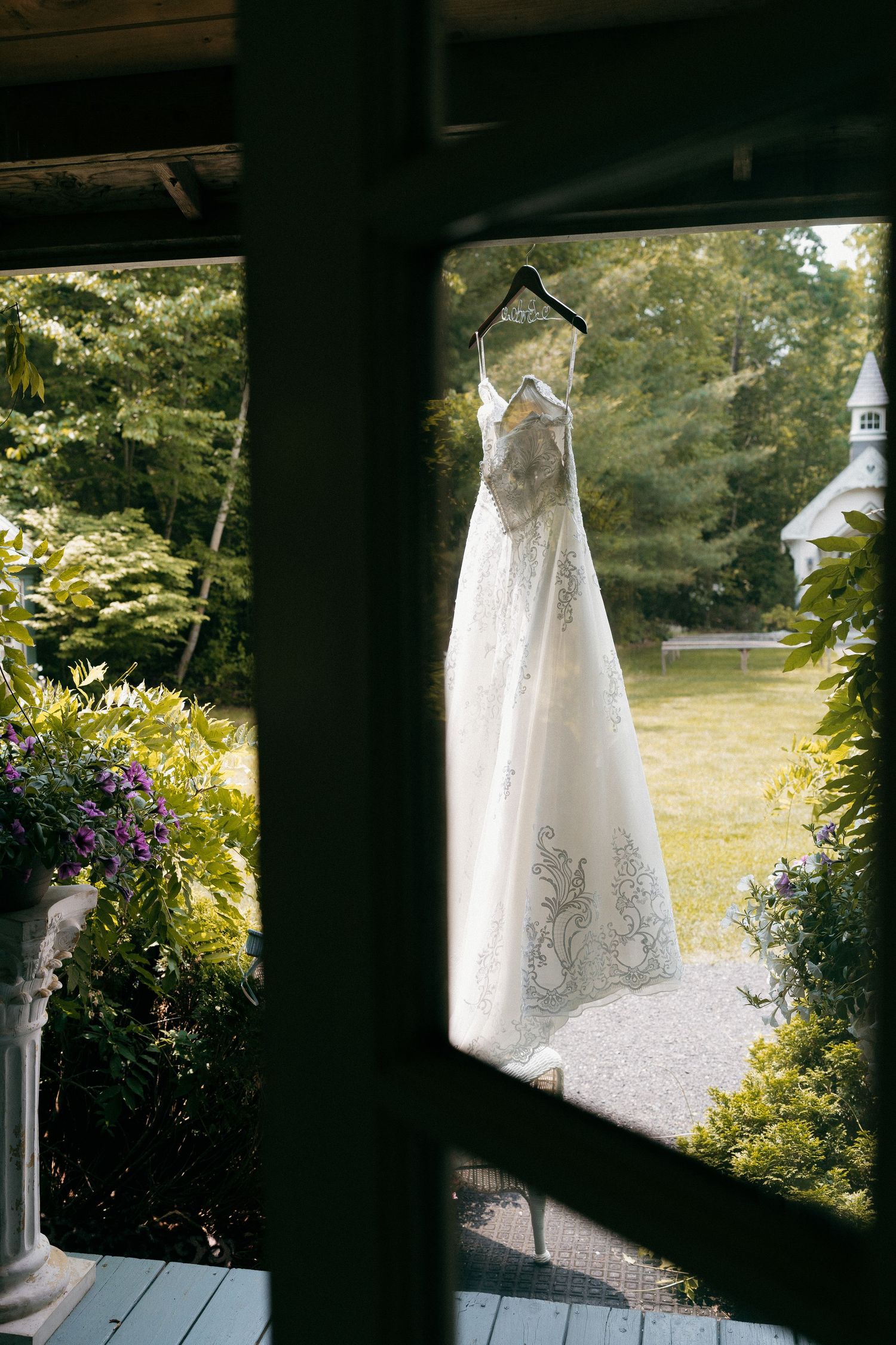 White wedding dress hanging on a porch with garden scenery in the background.