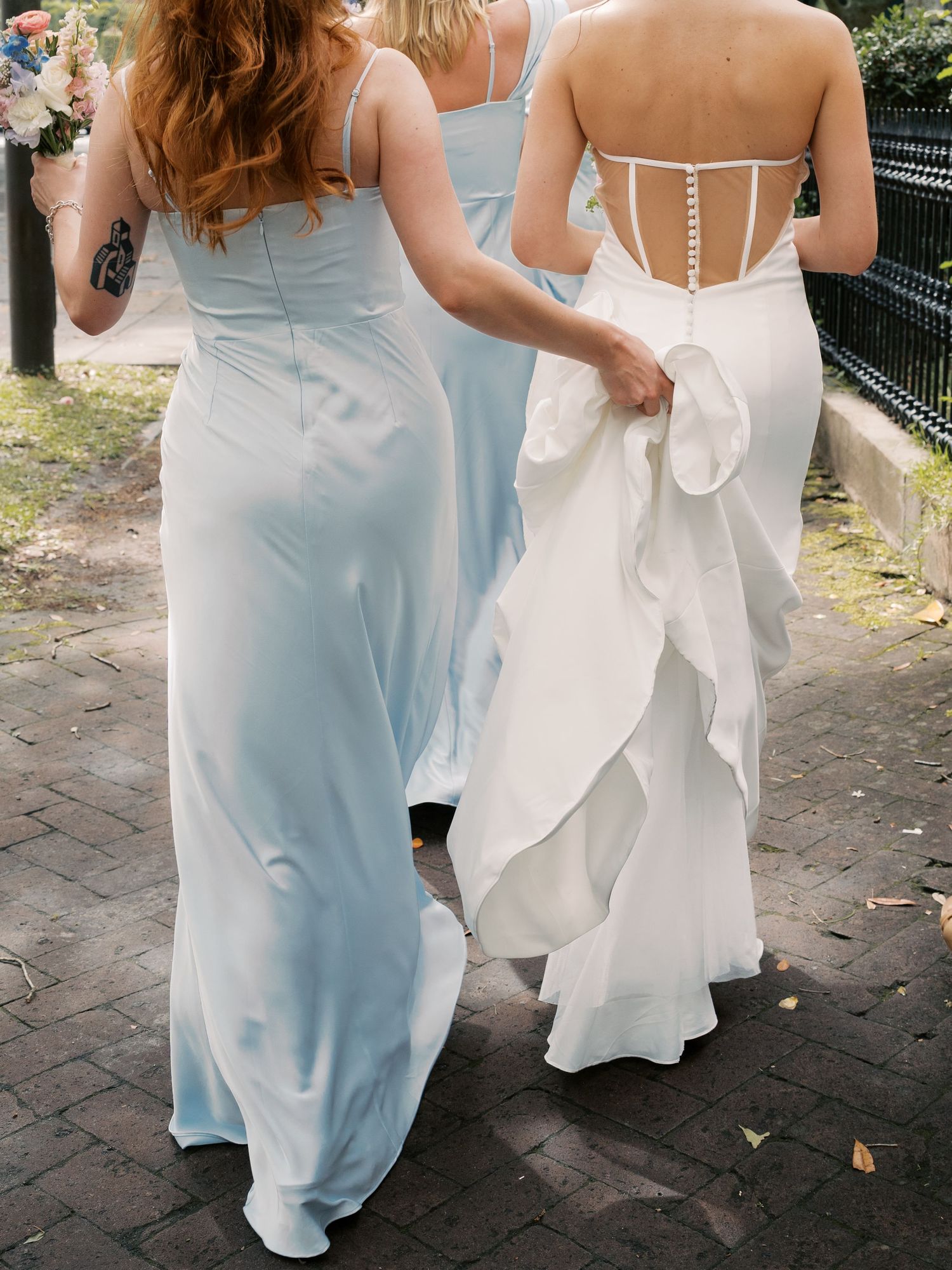 Wedding party walking along brick pathway showing flowing dresses in white and light blue.