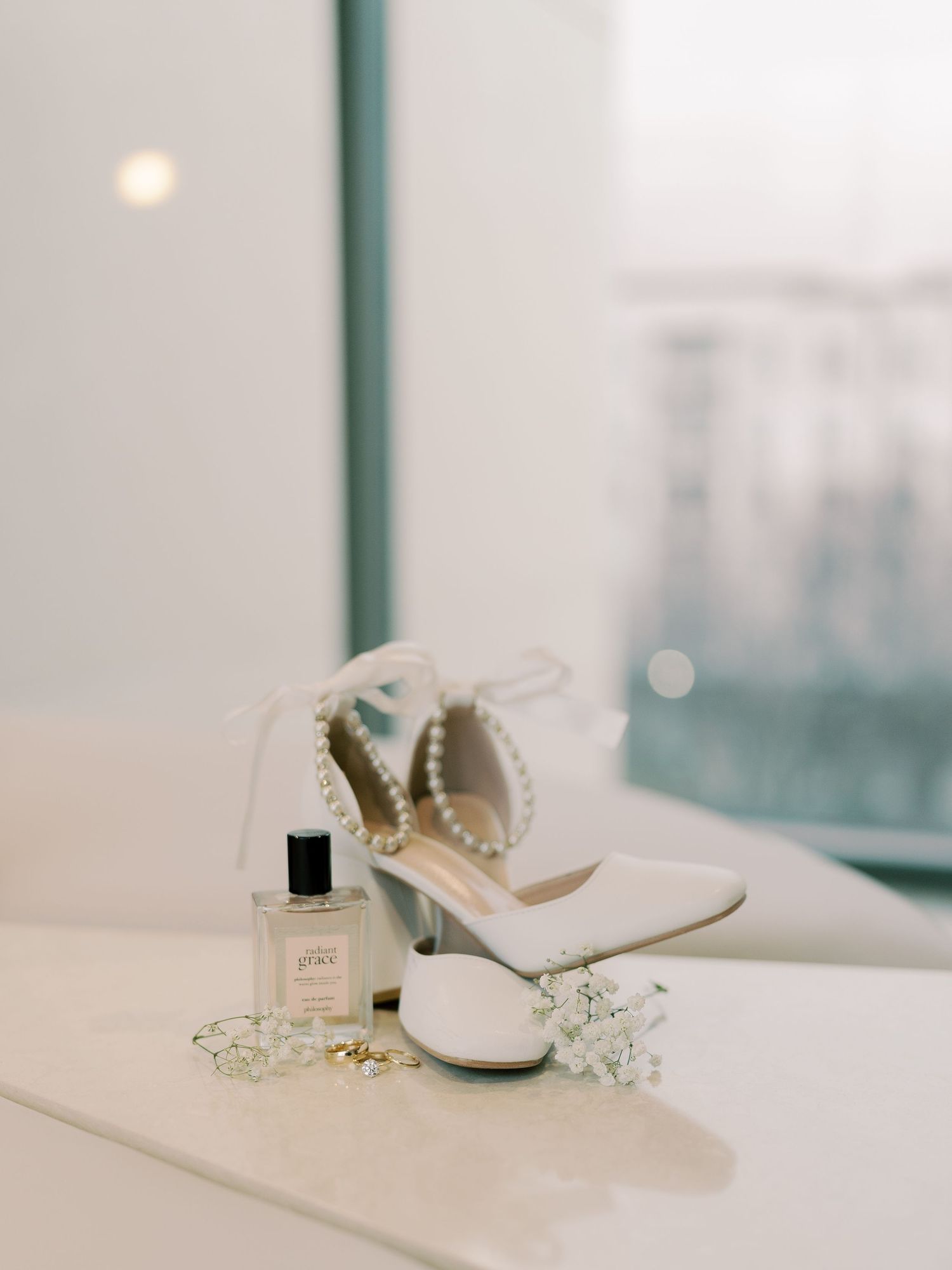 White bridal heels and accessories displayed on a light surface near a window.