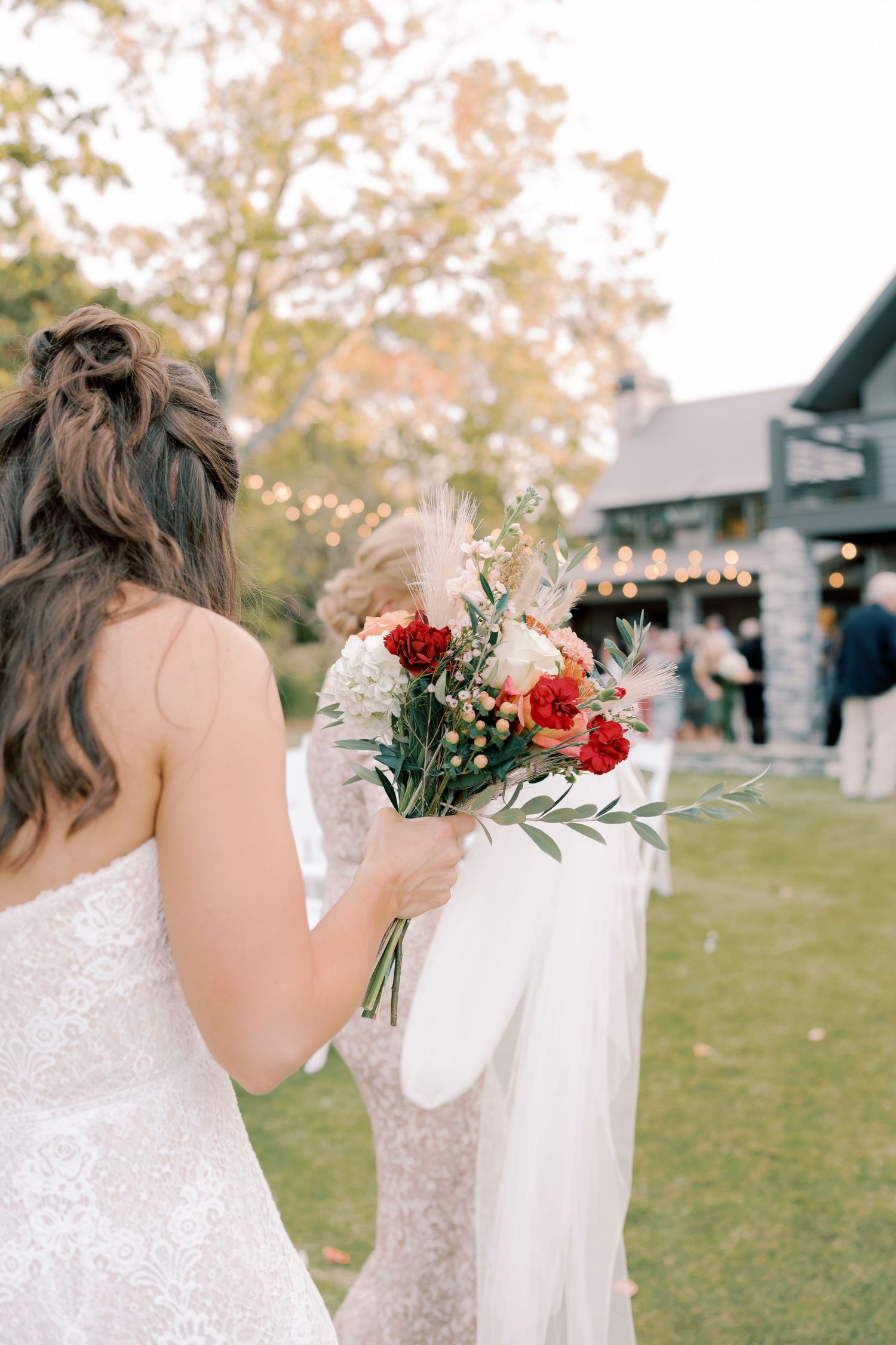 Close-up details of white lace wedding dress and bouquet with red and white flowers.