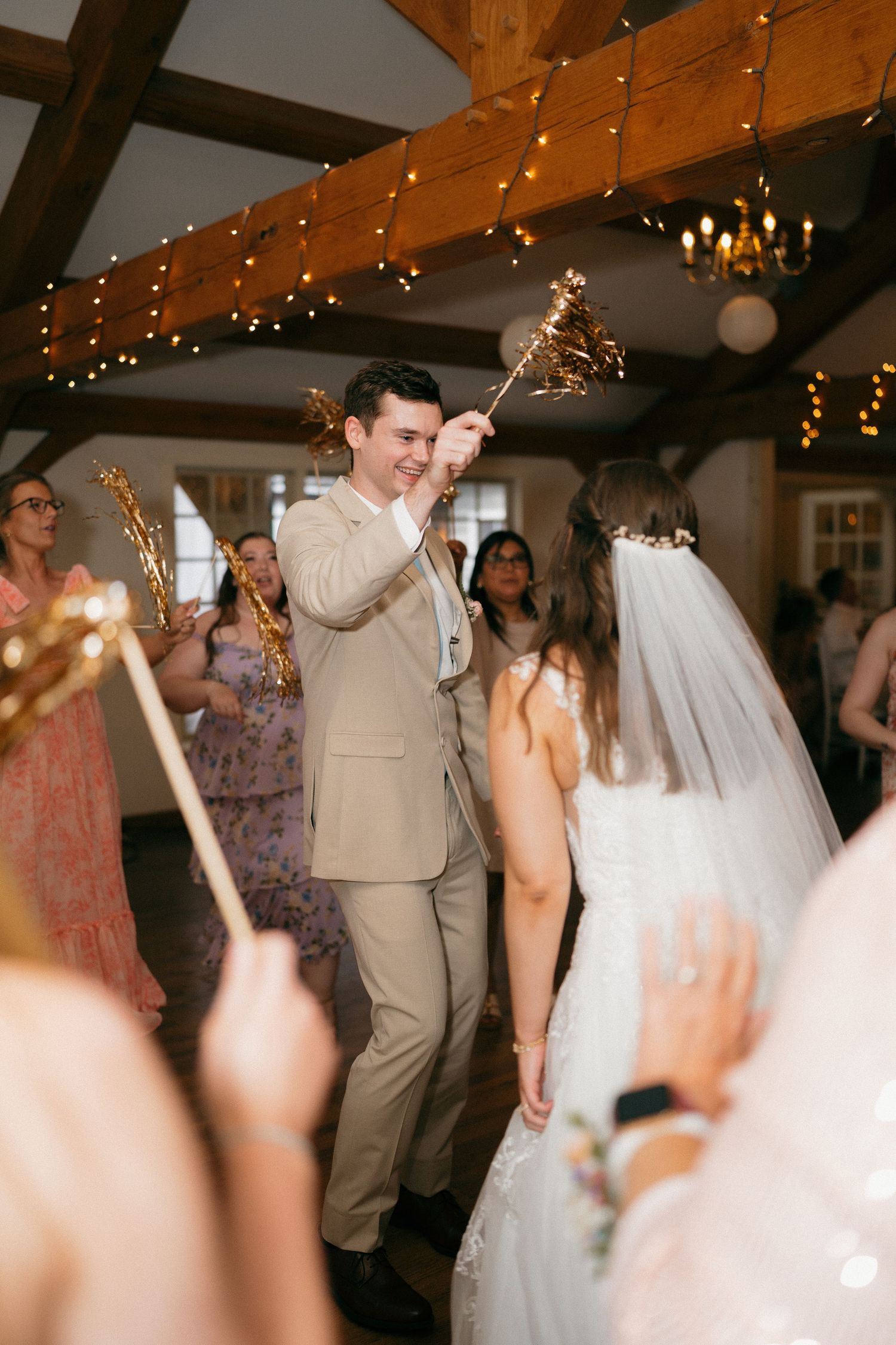 Wedding reception dance floor filled with guests under wooden beams and twinkling lights.