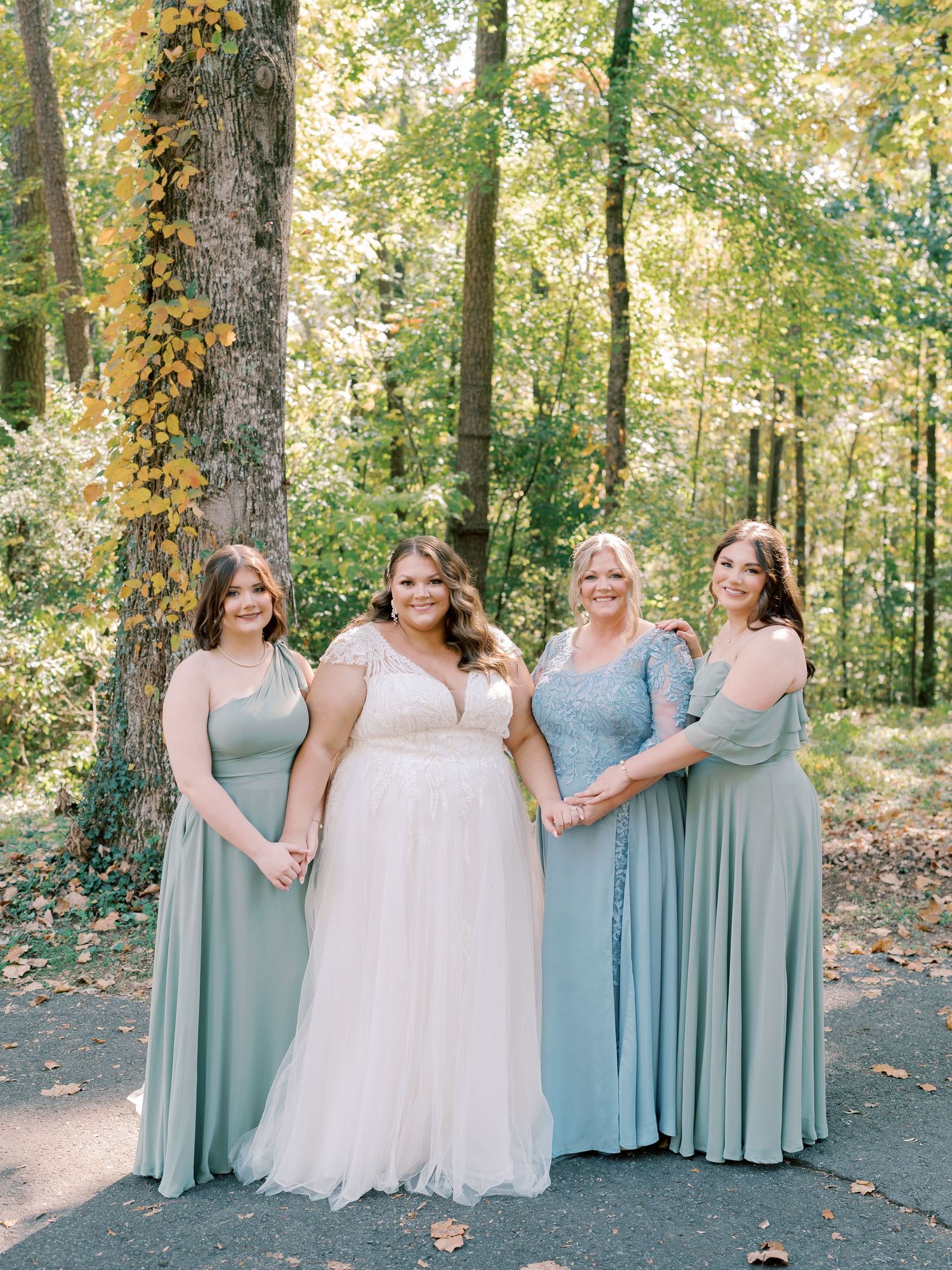 Bridal party in mint green dresses posing together outdoors with autumn trees in background.