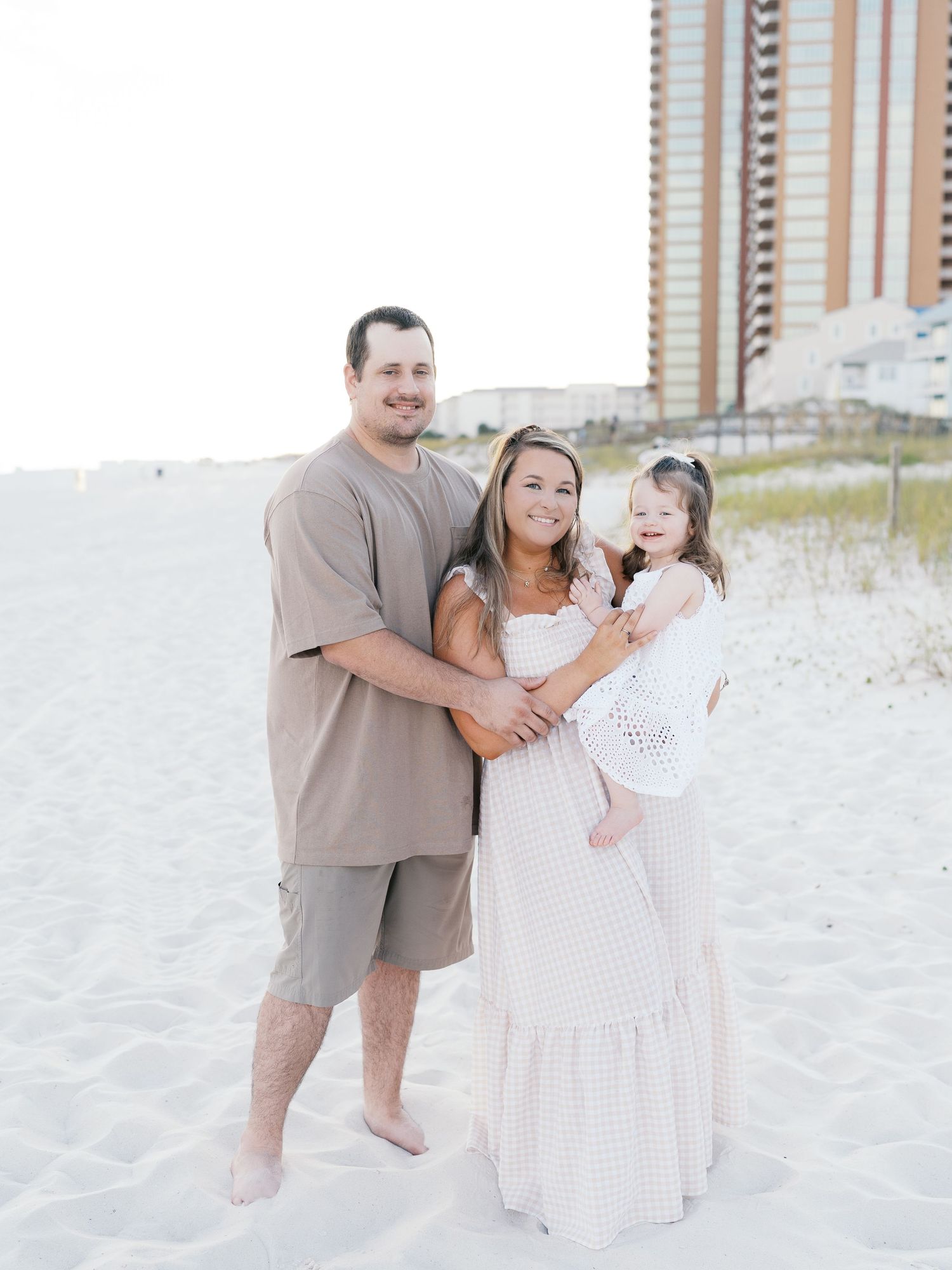 A family plays together on a pristine white sand beach with coastal buildings in the distance.