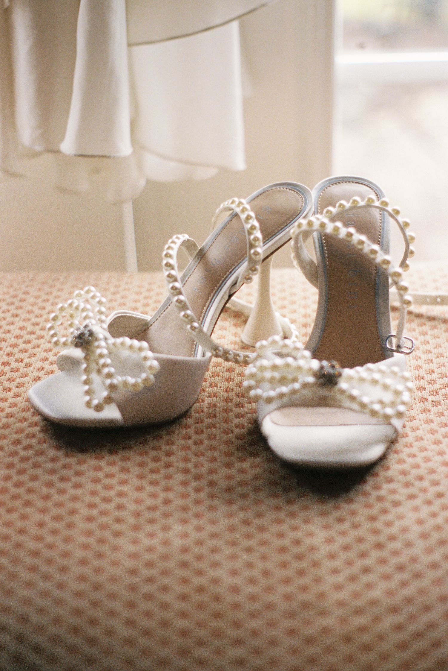 Elegant white bridal shoes with pearl details on polka dot fabric.