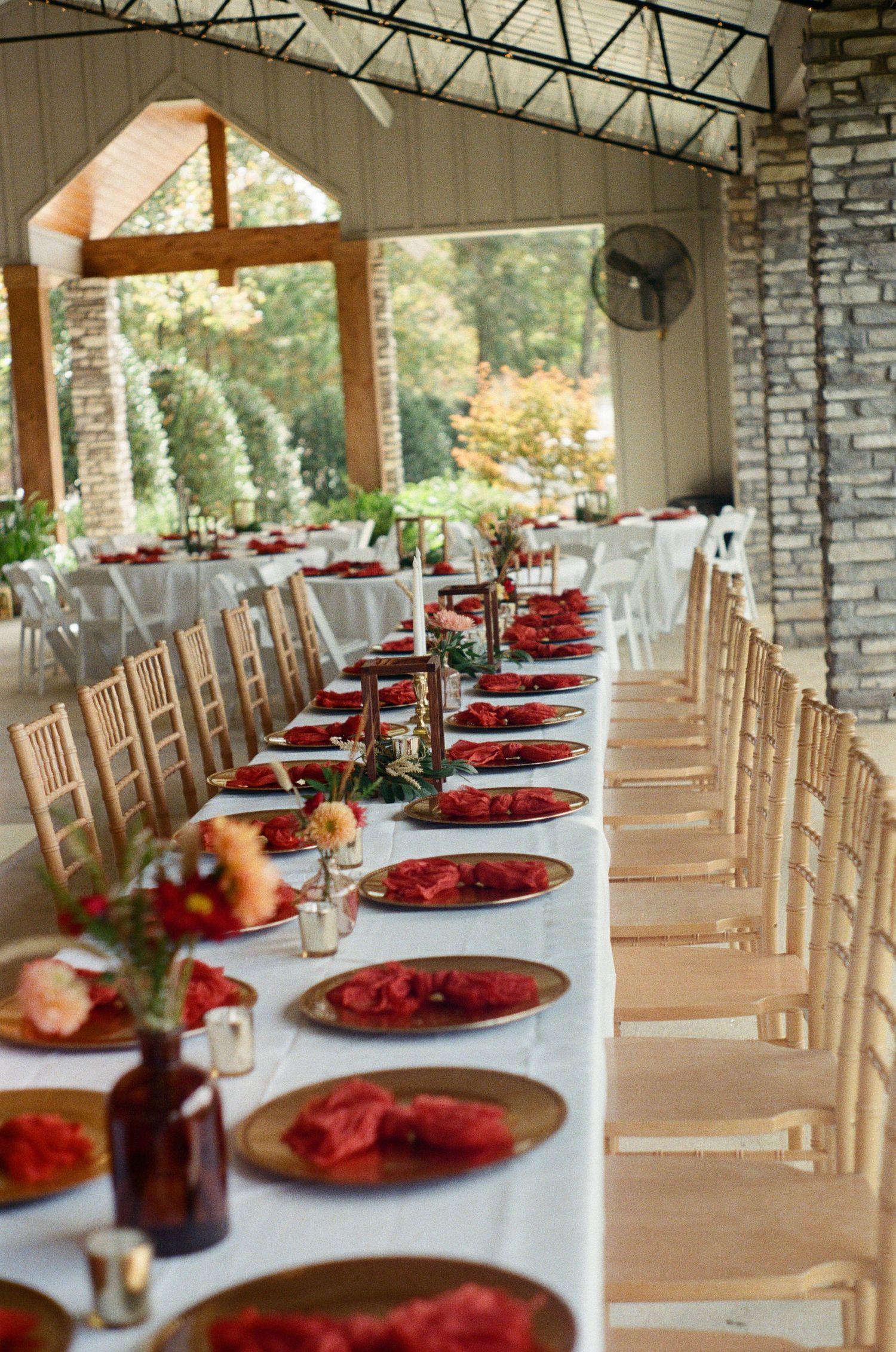 Long banquet tables set with red chargers and floral centerpieces in a stone-walled reception venue.