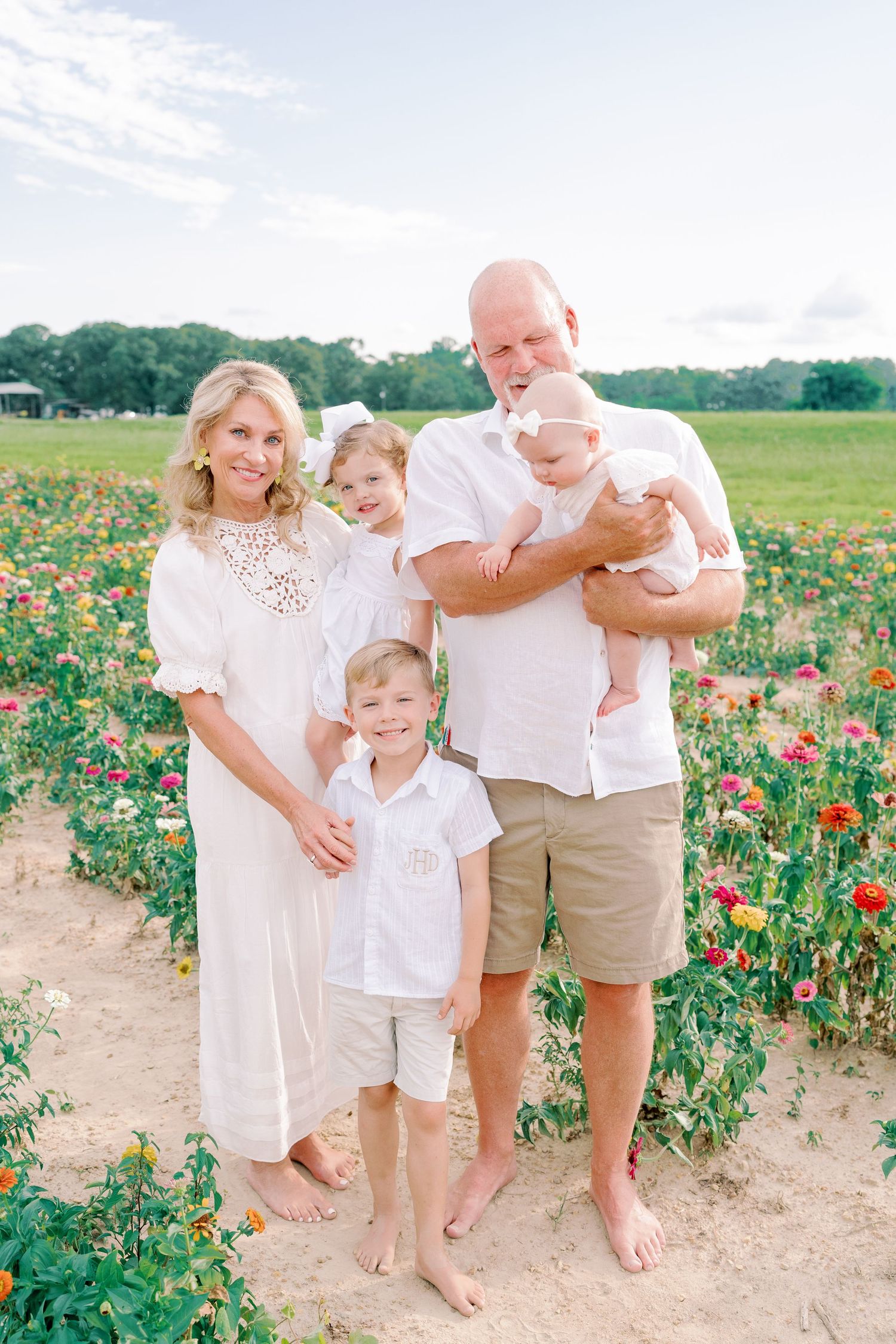 Family members in coordinated white and khaki outfits interact playfully in a flower field.