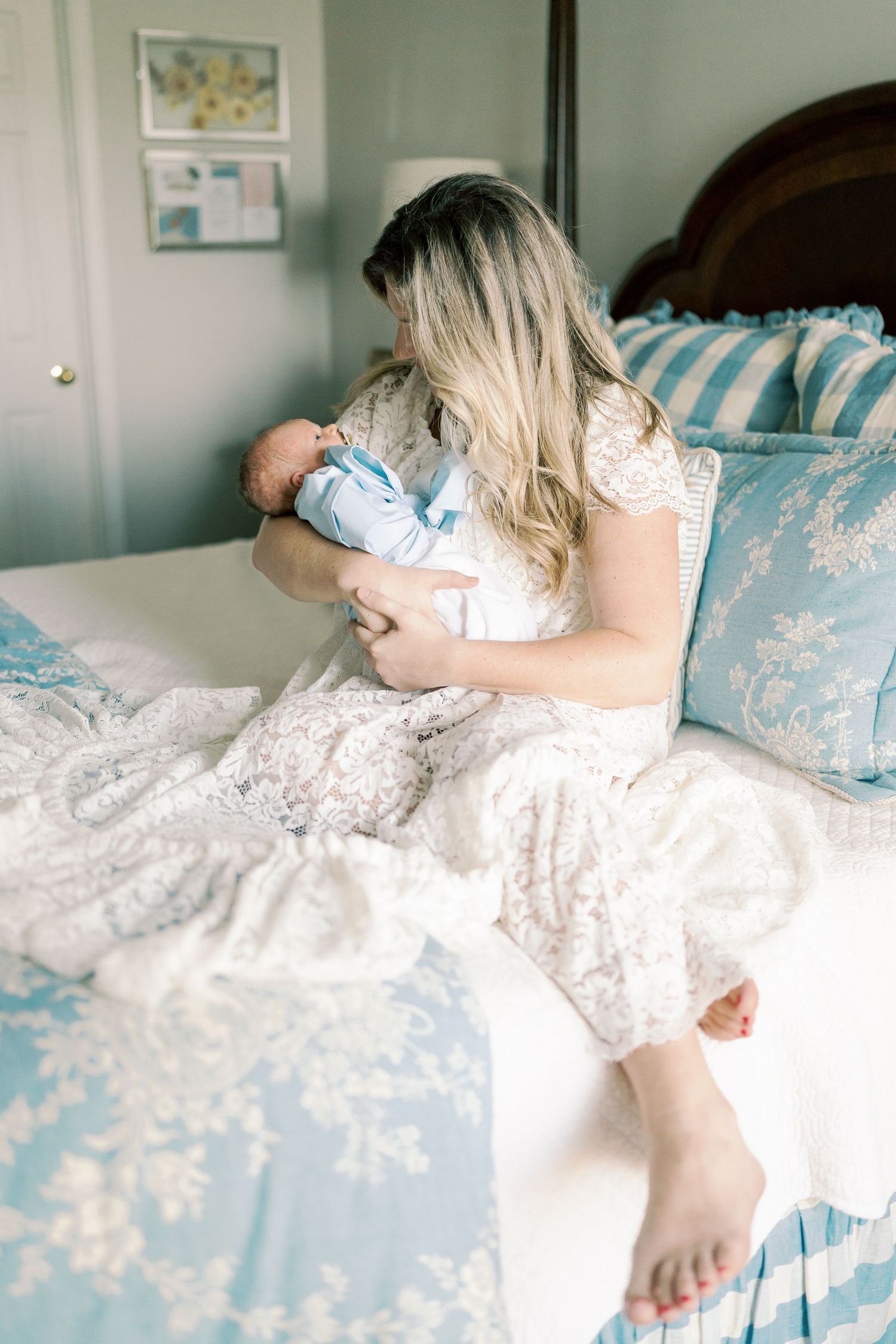 Mother rests with newborn on bed with blue and white decor.