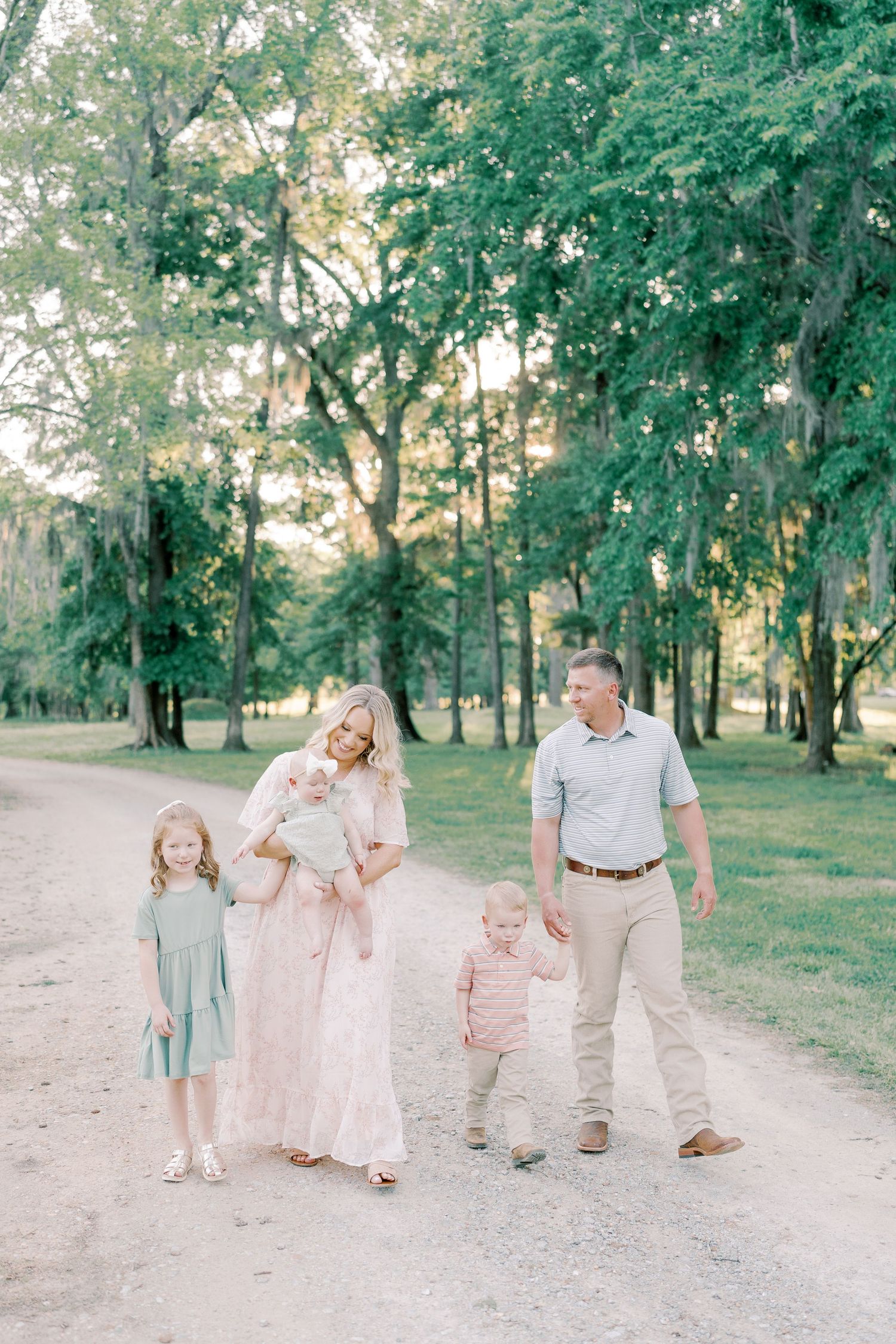 Family members stroll together on a tree-lined dirt path during golden hour.